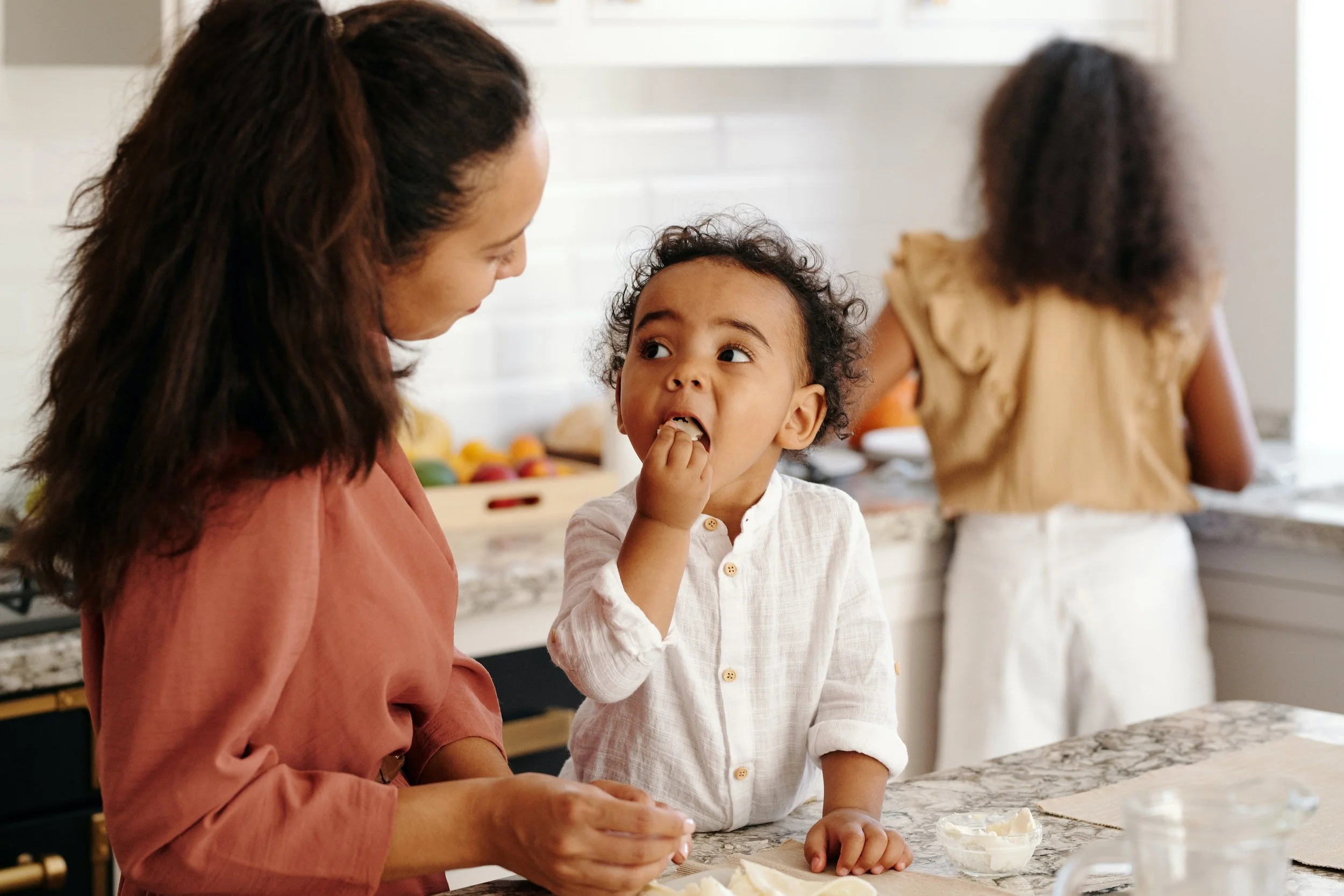 Woman and child having a conversation in a kitchen with a girl in the background.