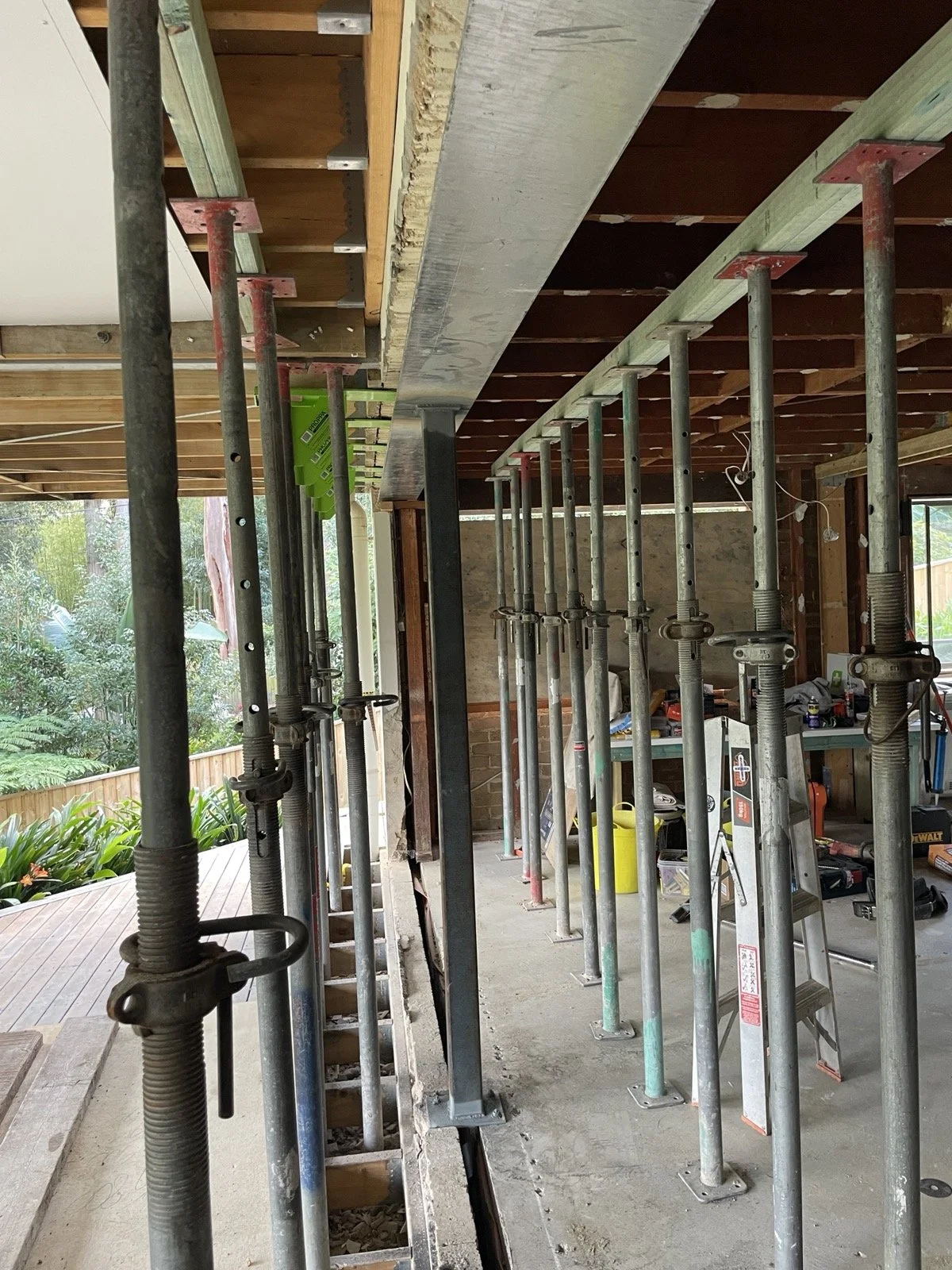 Construction site with metal support beams and scaffolding inside a house, unfinished walls, and construction tools and materials visible.