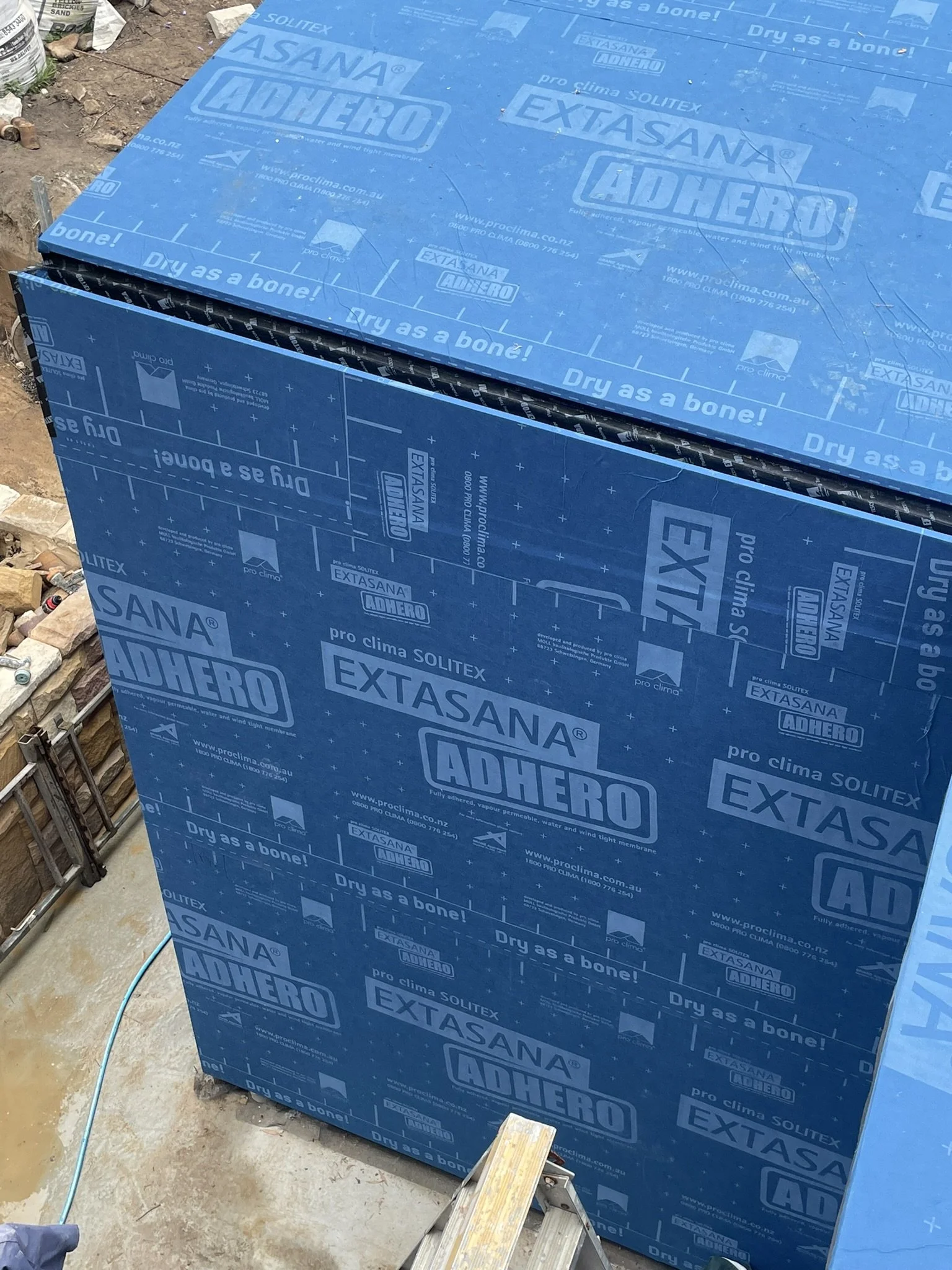 Blue building insulation material with branding and the slogan 'Dry as a bone!' at a construction site.
