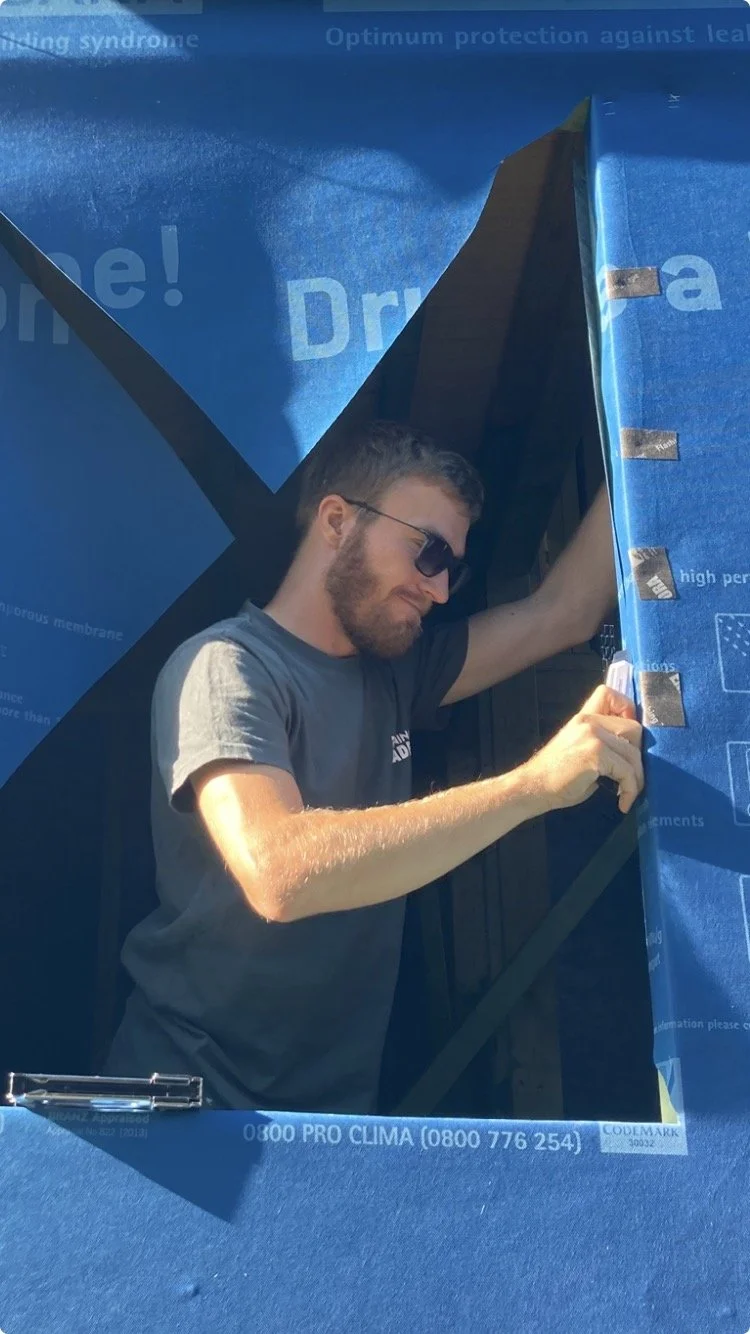 A man with sunglasses and a beard installing weather membrane around window opening