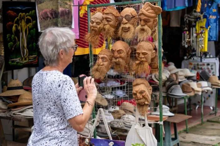 A woman browsing a market stall with handcrafted clay heads and hats.