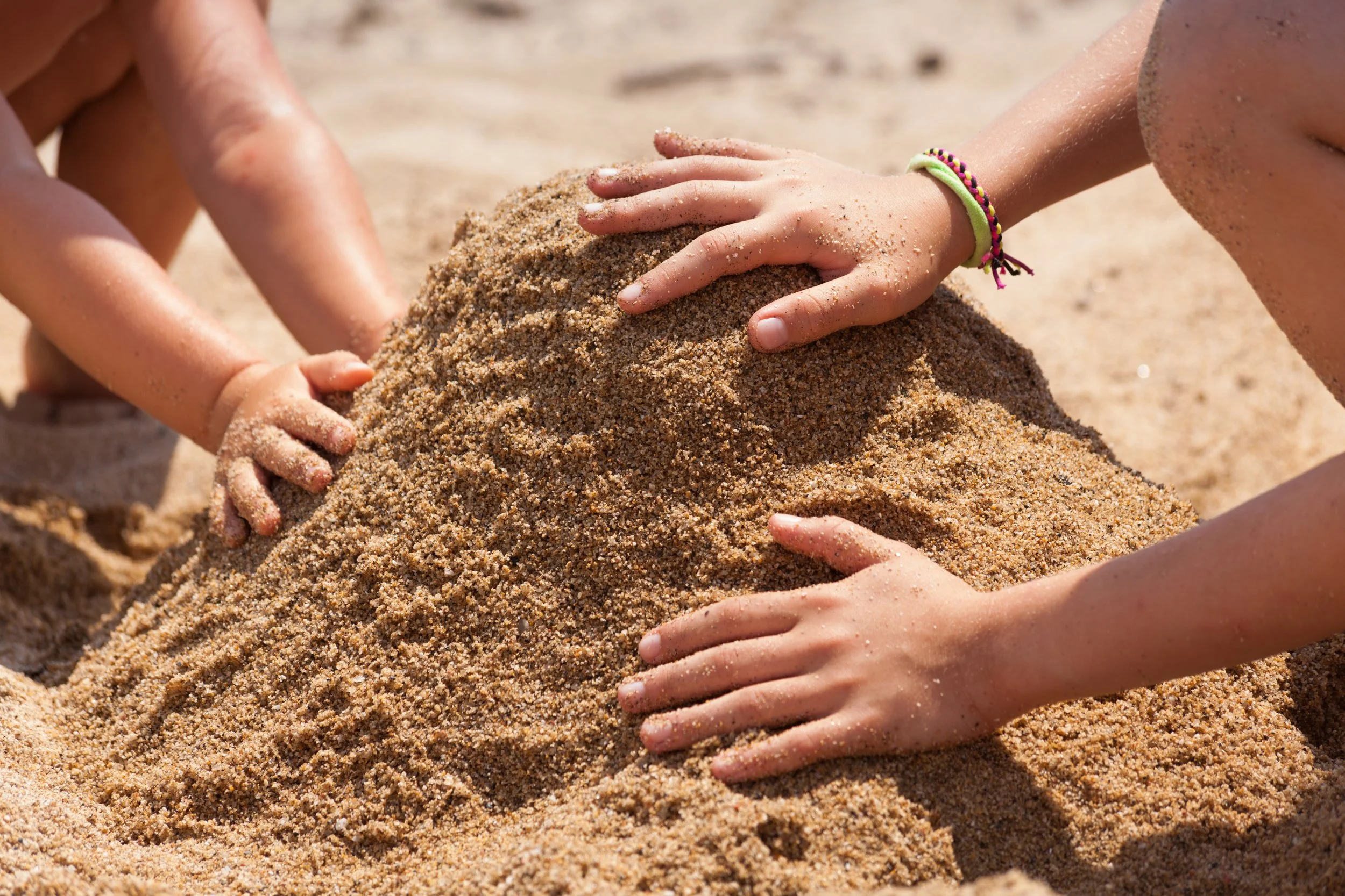 Children playing in sand on a beach, building a sandcastle with their hands.