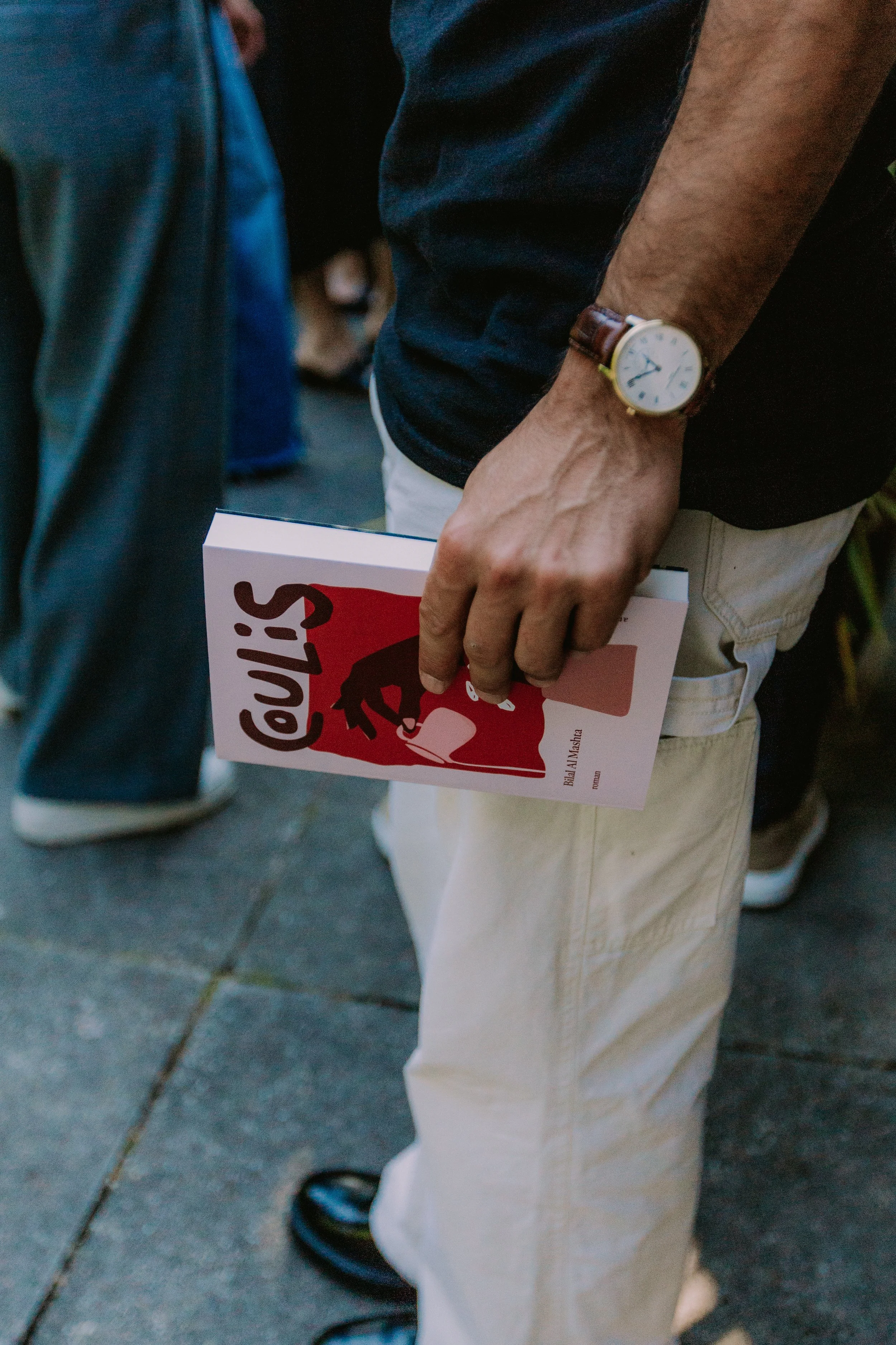 Person holding a book with a red and white cover titled 'COULIS' at an outdoor event.
