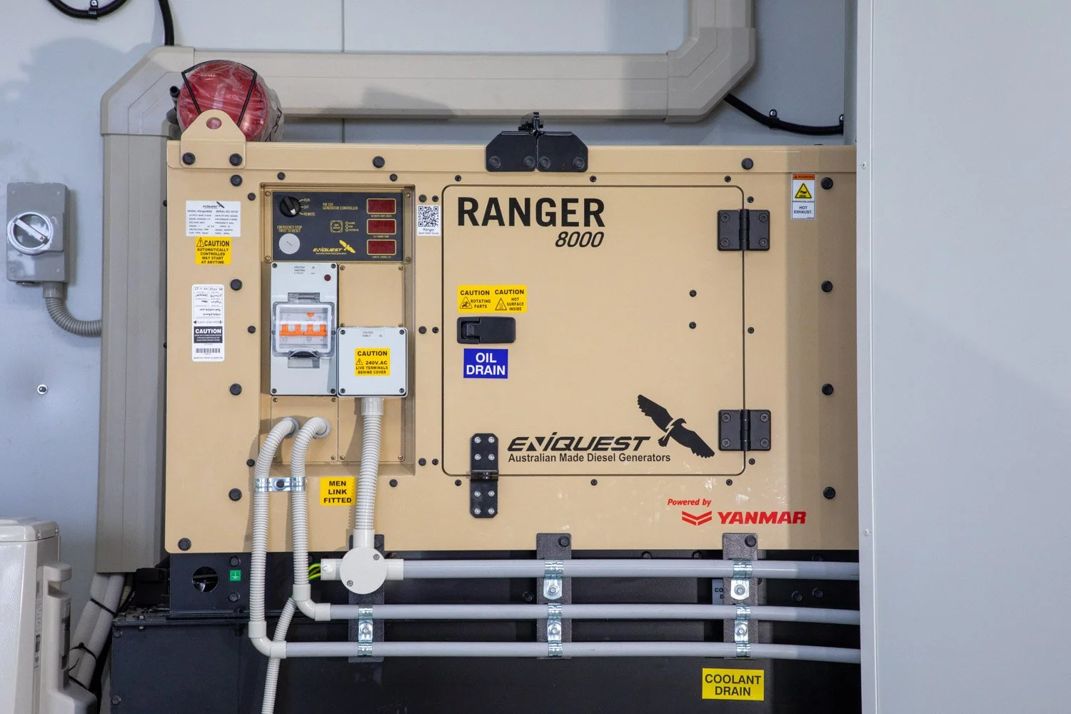 An Australian ENIQUEST diesel generator labeled 'RANGER 8000' powered by Yanmar, installed with caution stickers, oil drain and coolant drain pipes, electrical connections, and warning labels.