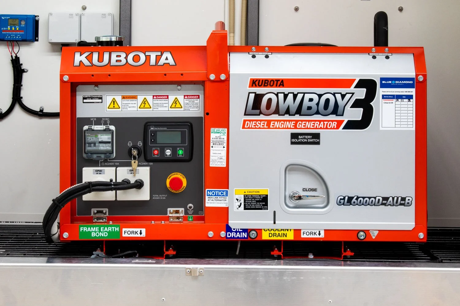 Red Kubota Lowboy diesel engine generator with control panel, warning labels, and labels indicating grounding and drainage points, situated on a metal platform.
