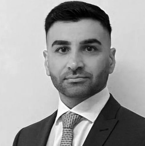 Schwarz-weiß Porträt eines Mannes in einem Anzug mit Krawatte, mit dunklem, kurzgeschnittenem Haar, vor hellem Hintergrund.