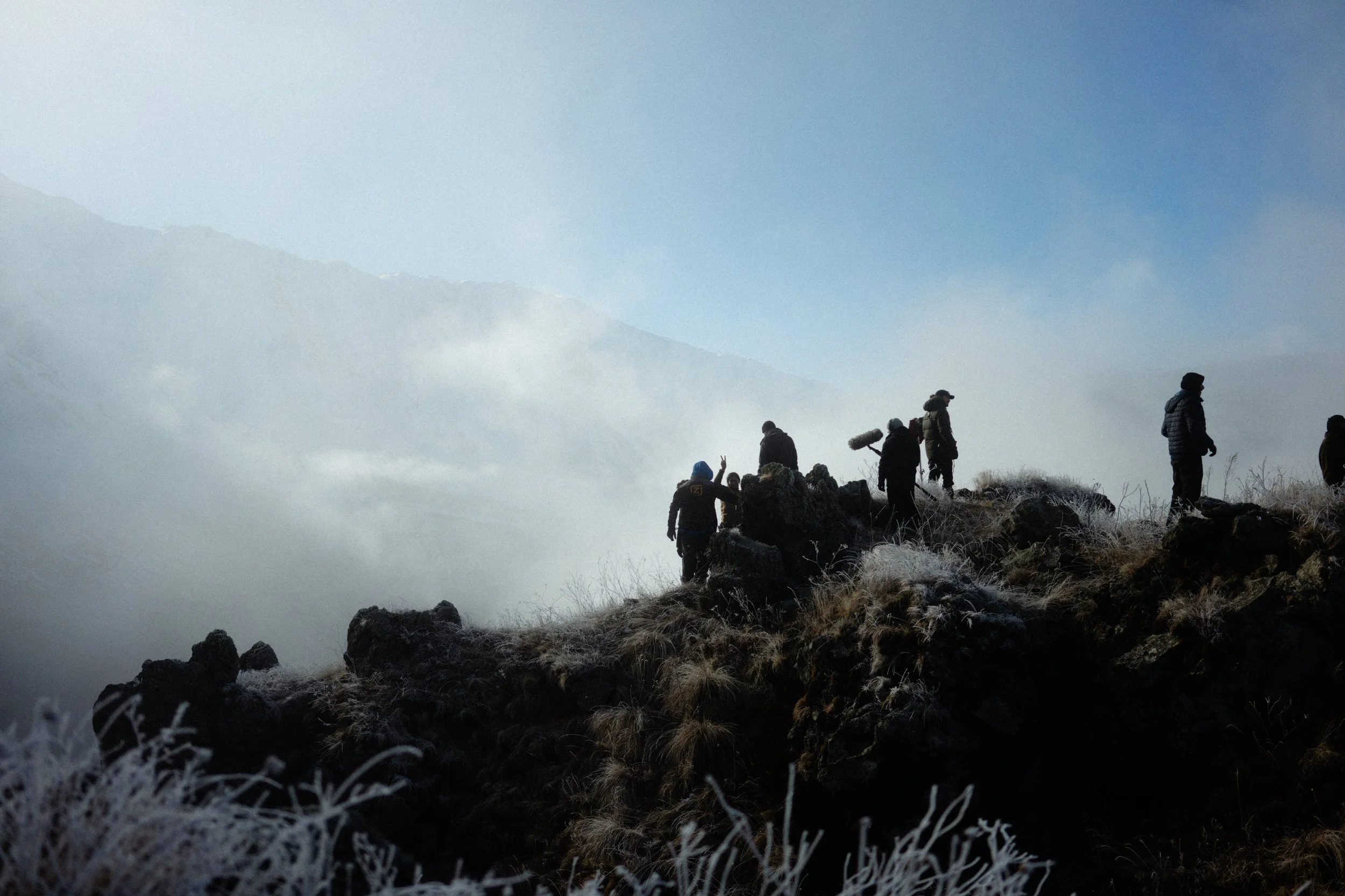 A group of hikers walking along a rocky, frosty terrain on a mountain trail with mist and clouds in the background.