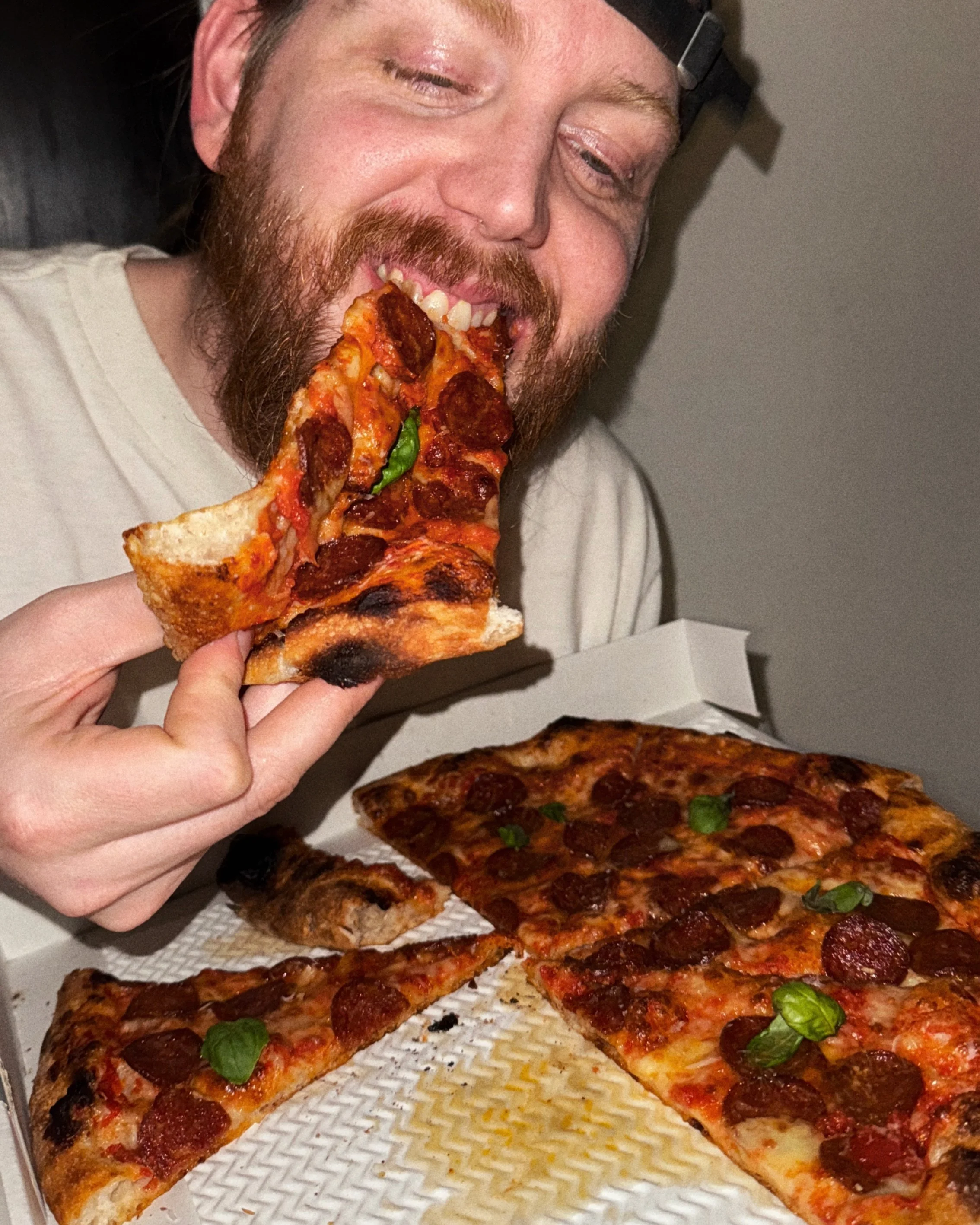 person taking a bite from a crispy new york style pepperoni pizza