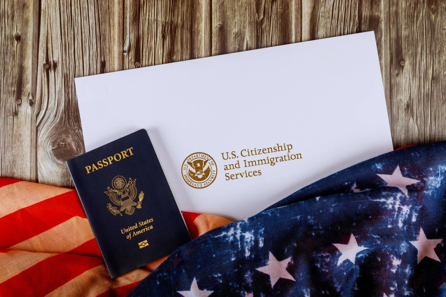 U.S. citizenship and immigration services envelope, American flag, and U.S. passport on a wooden surface.
