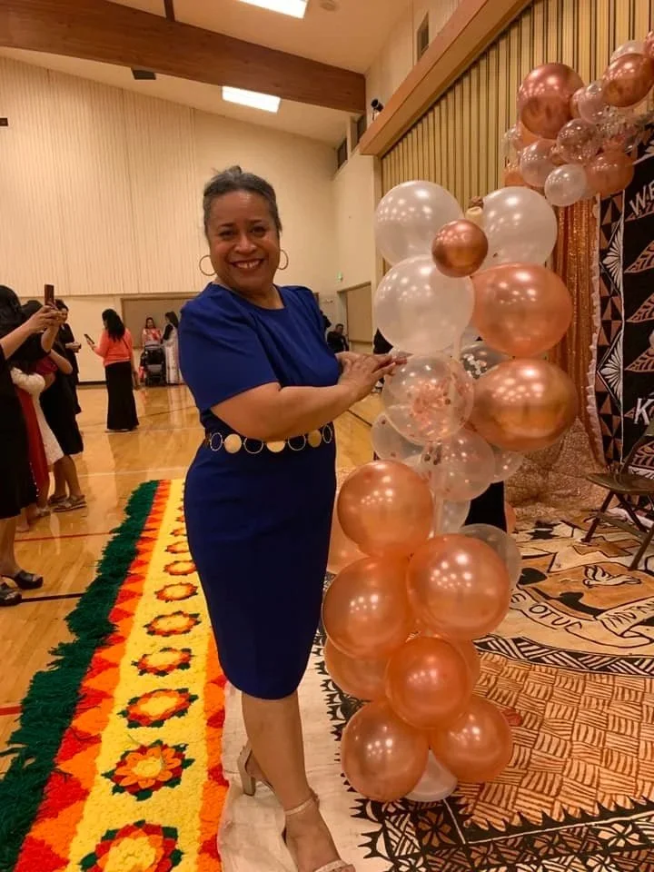 woman in blue dress smiling at a balloon decoration at an indoor event.