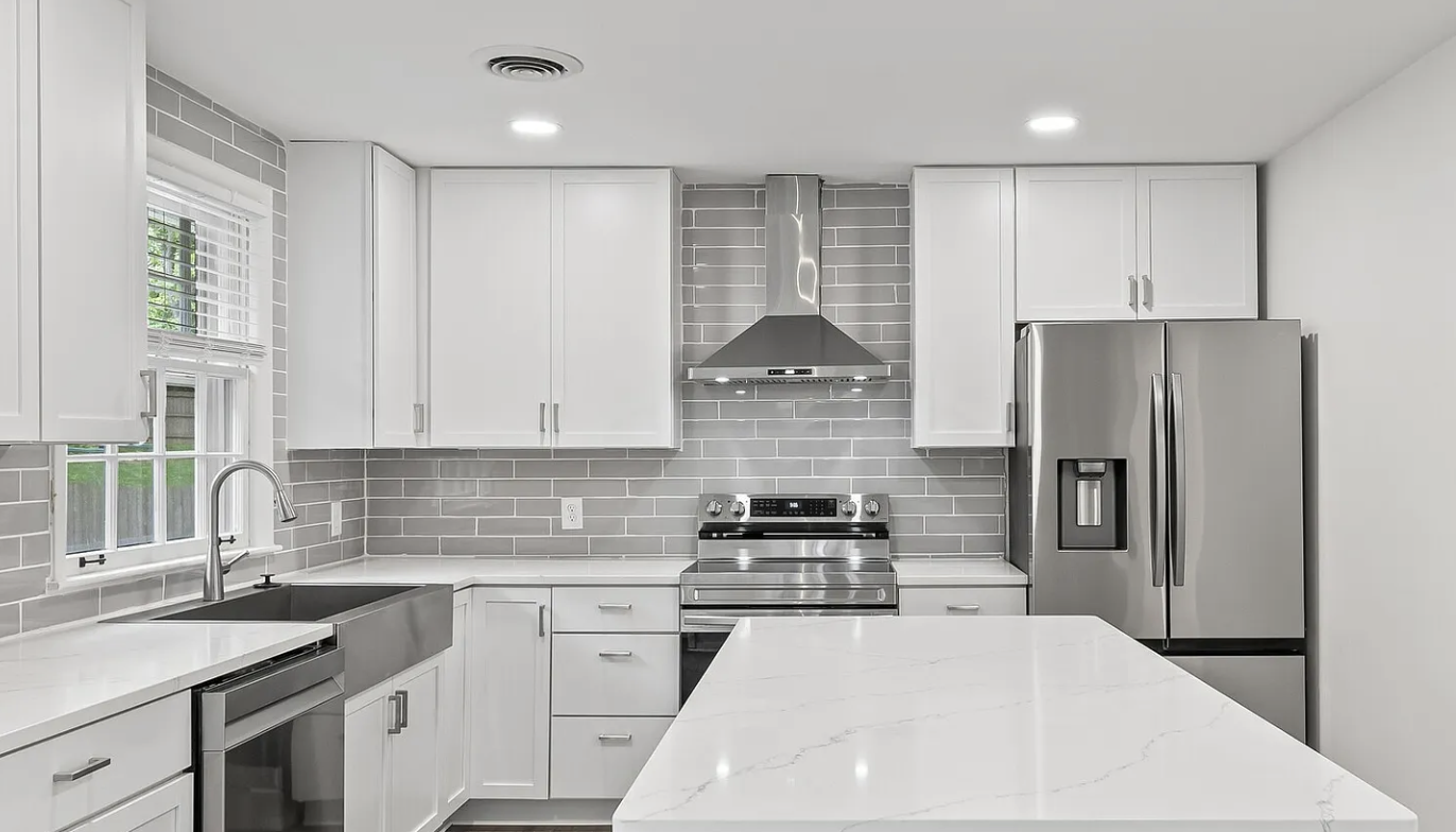 Modern kitchen with white cabinets, gray subway tile backsplash, stainless steel appliances, and a large white marble countertop island.