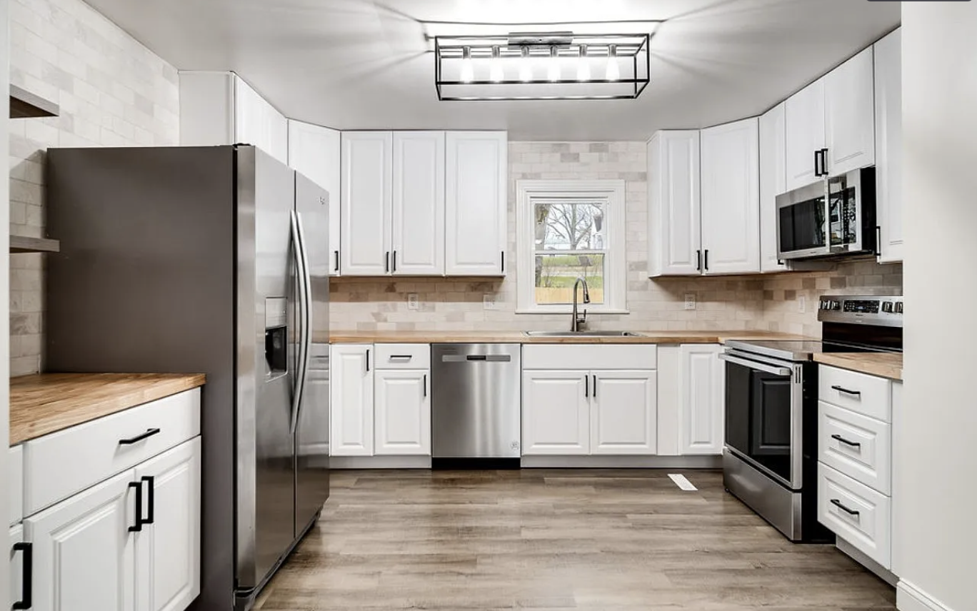 Modern kitchen with white cabinets, stainless steel appliances, a small window over the sink, and a wood countertop.