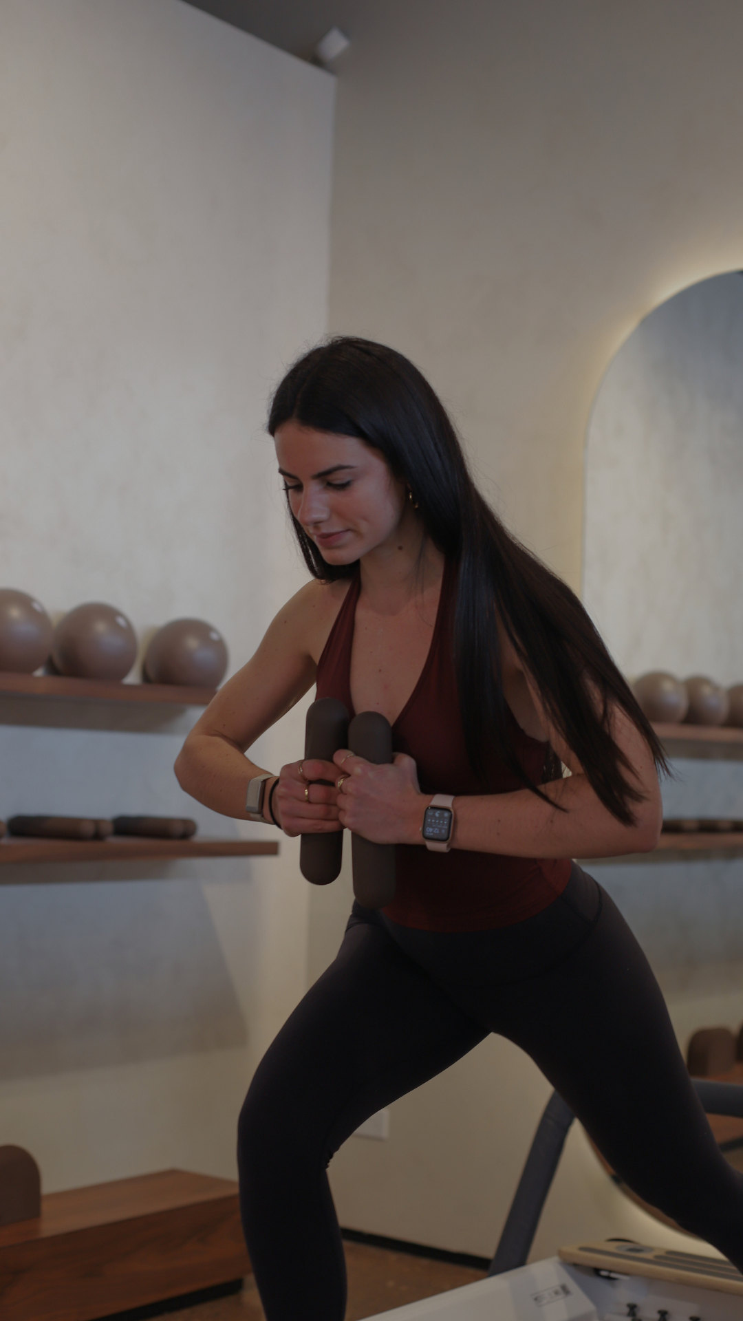 A woman in workout attire holding dumbbells in a fitness studio.