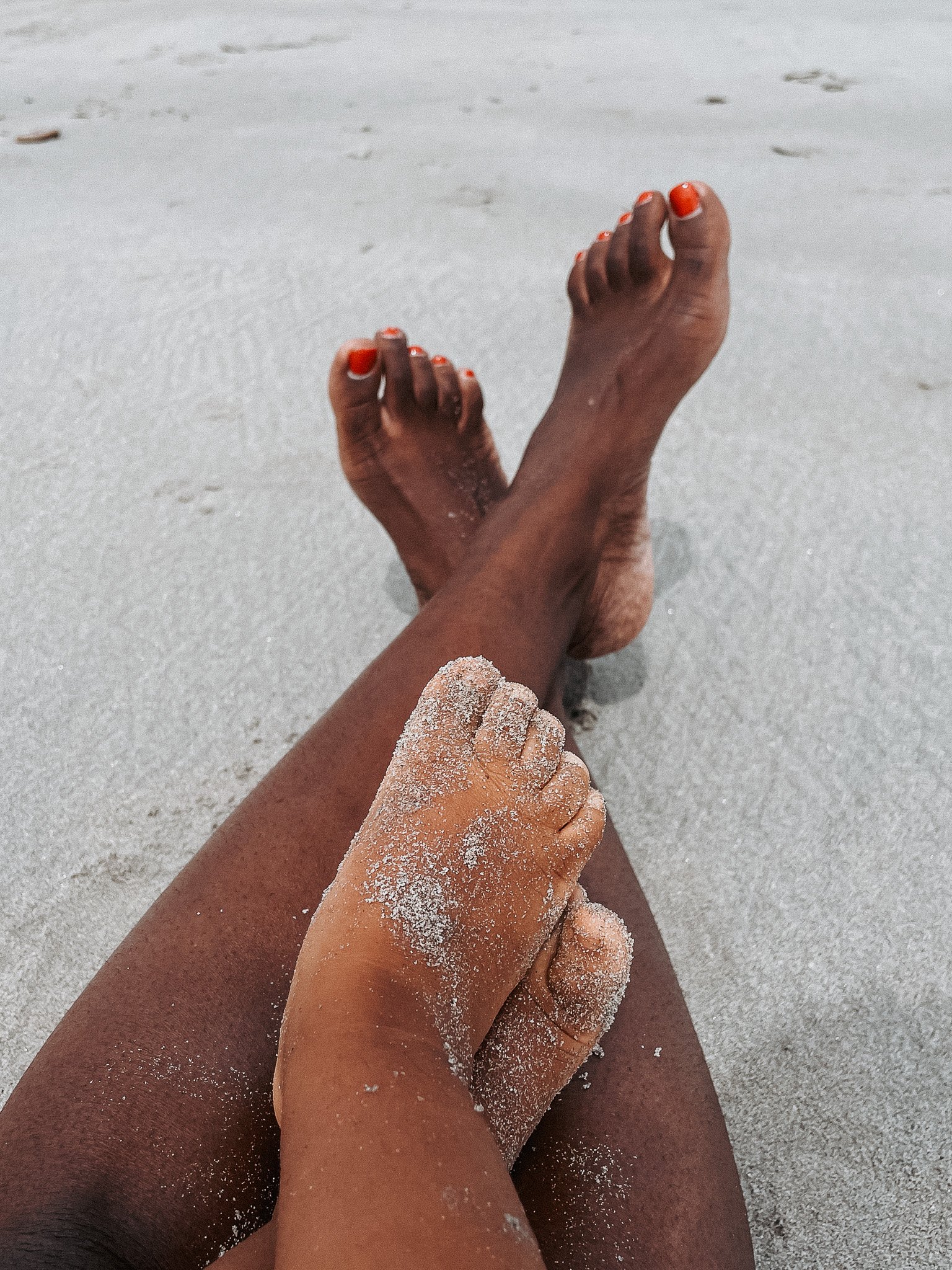 People relaxing on a sandy beach with feet and hand covered in sand.