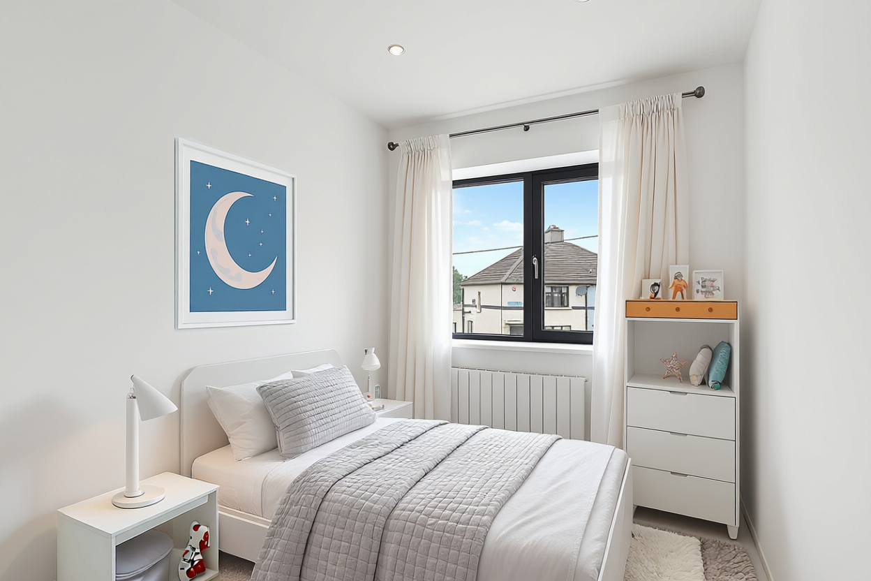 A bedroom with white walls, a window with cream curtains, a white bed with gray bedding, a white nightstand with a lamp, and a white dresser with decorative items and framed pictures, and a moon and stars wall art.