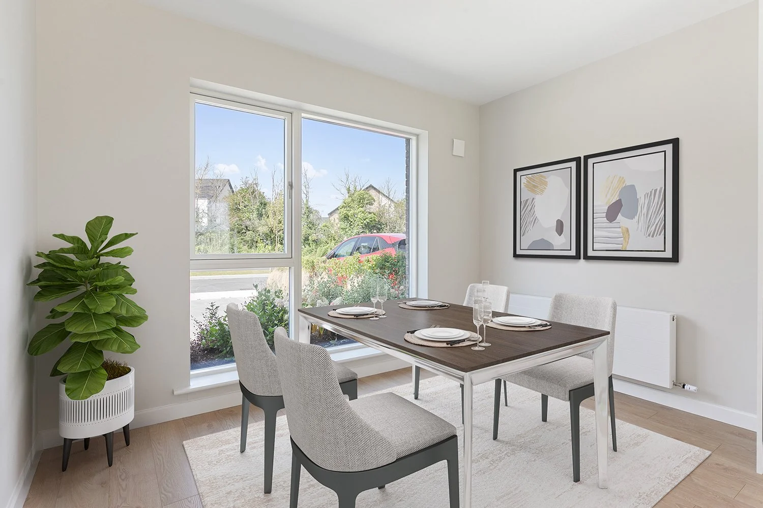 Modern dining room with a wooden table set with plates and glasses, six padded chairs, a large window, abstract artwork on the wall, a potted plant, and a neutral-colored area rug.