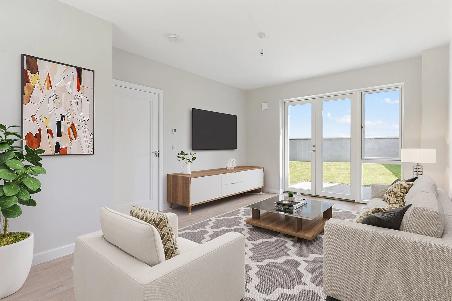 Modern living room with beige sofas, a glass coffee table, a patterned rug, a large potted plant, and a wall-mounted TV, with a view of a backyard through glass doors.