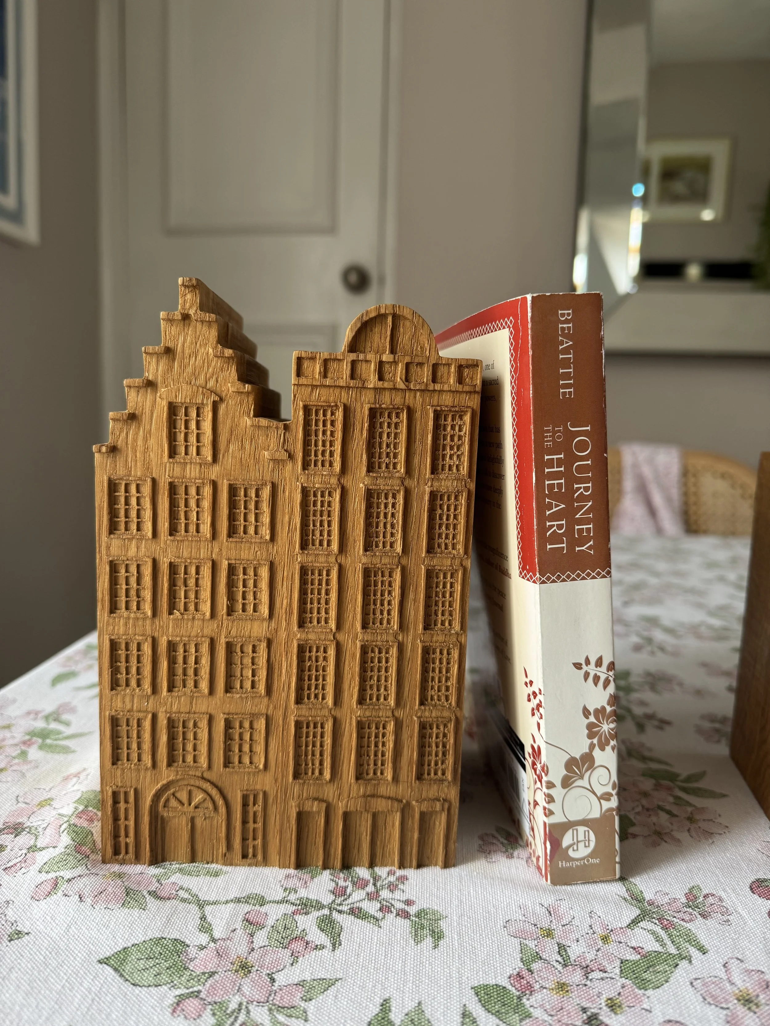 Wooden planters shaped like buildings placed on a floral tablecloth, with a book titled "Journey to the Heart" by Beatles standing behind them.