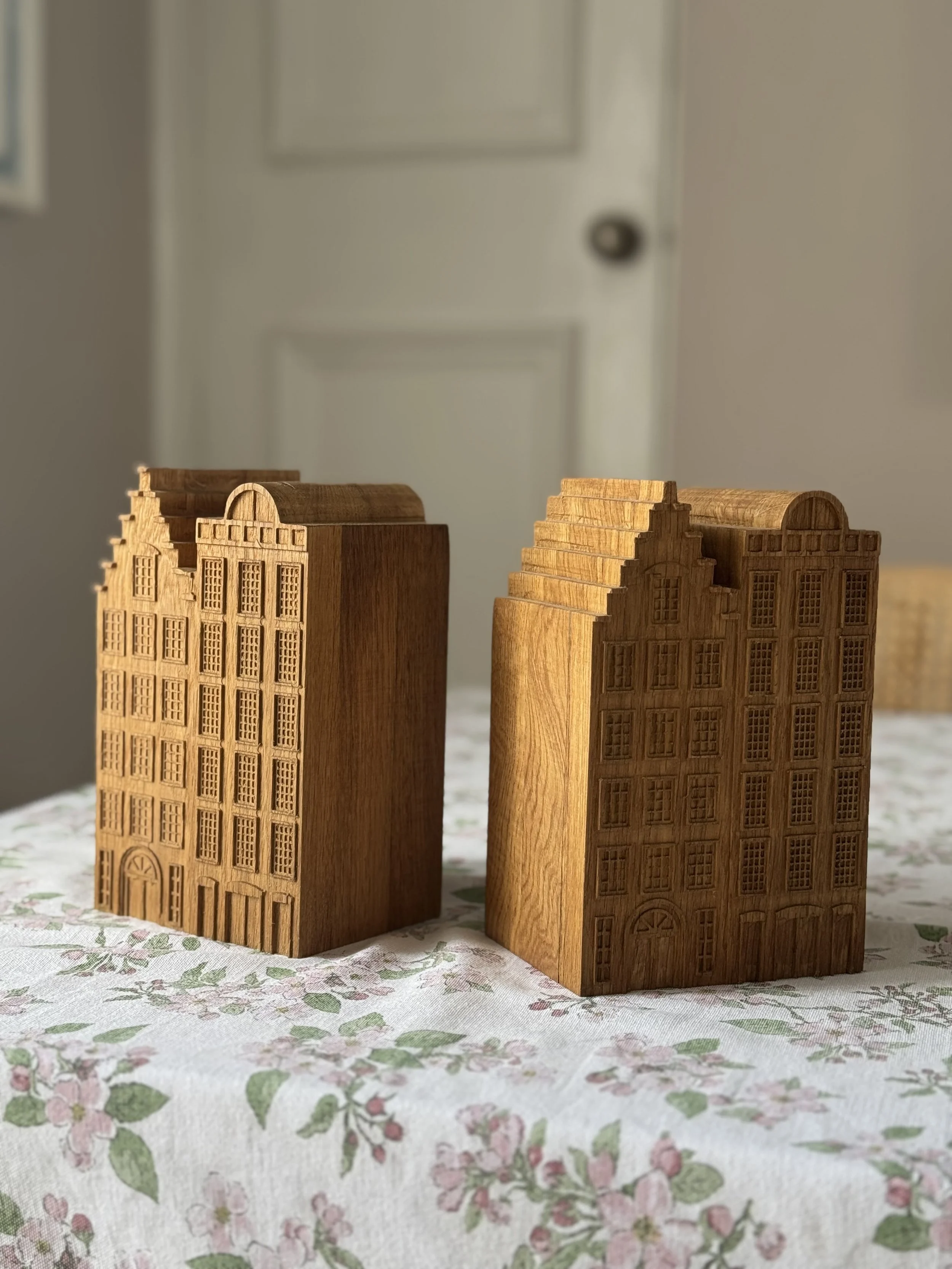 Two wooden houses with detailed windows and doors on a floral tablecloth.