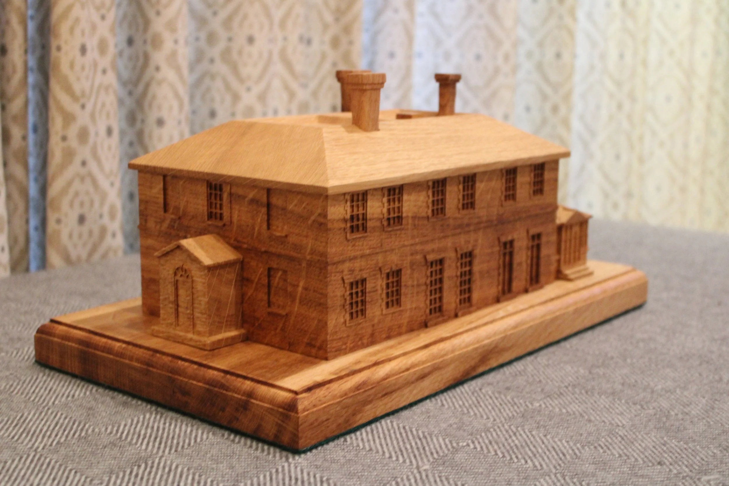 A detailed wooden model of a large, classical-style building with multiple floors and a prominent hipped roof, set on a wooden base.