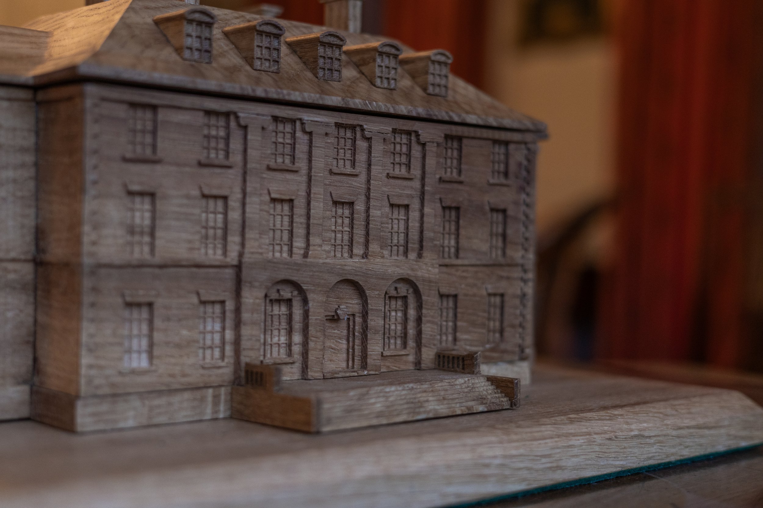 A detailed wooden model of a classic multi-story building with multiple windows, stairs, and a archway entrance.
