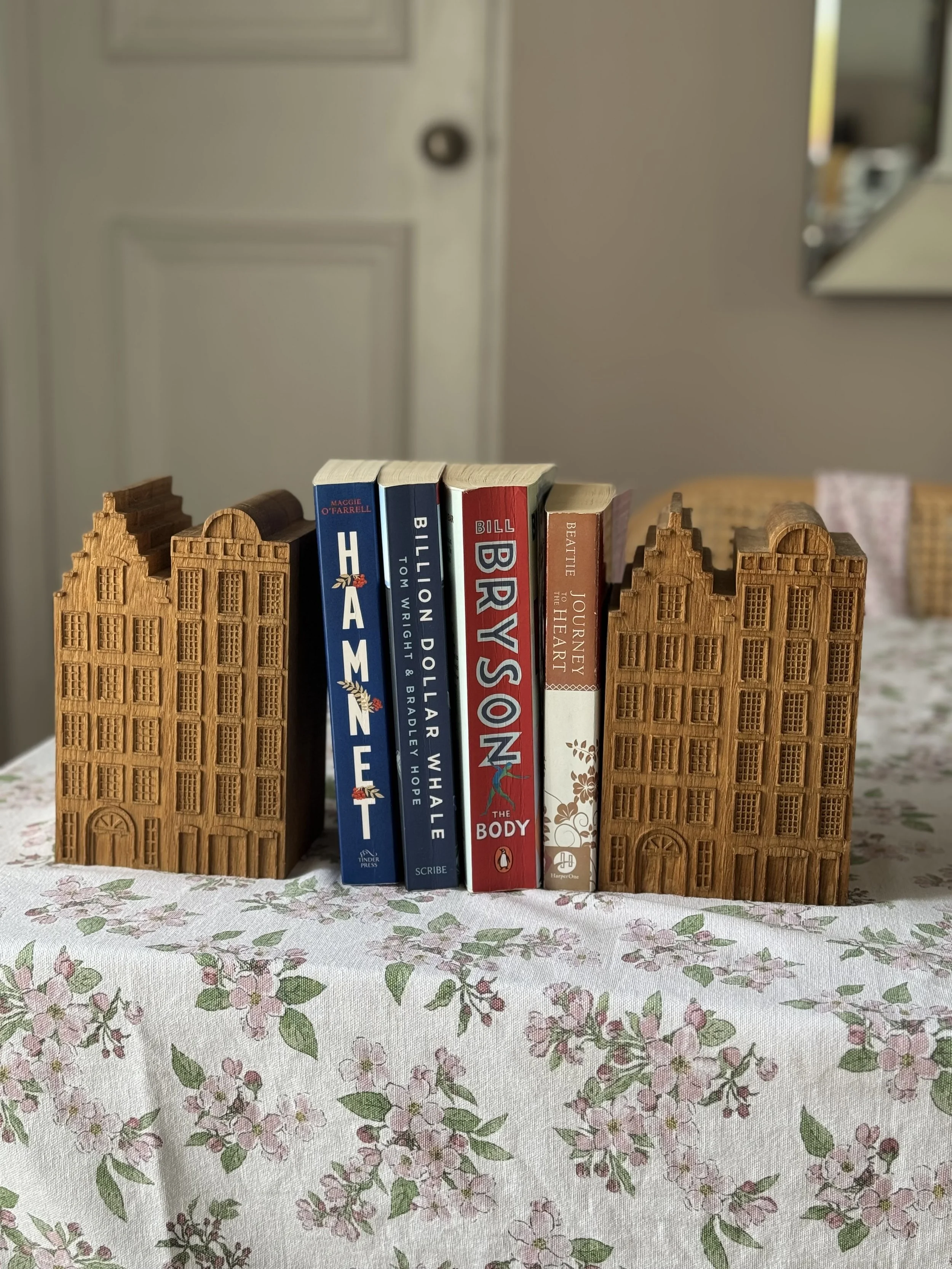 Four books standing upright between two decorative wooden building models on a floral tablecloth.