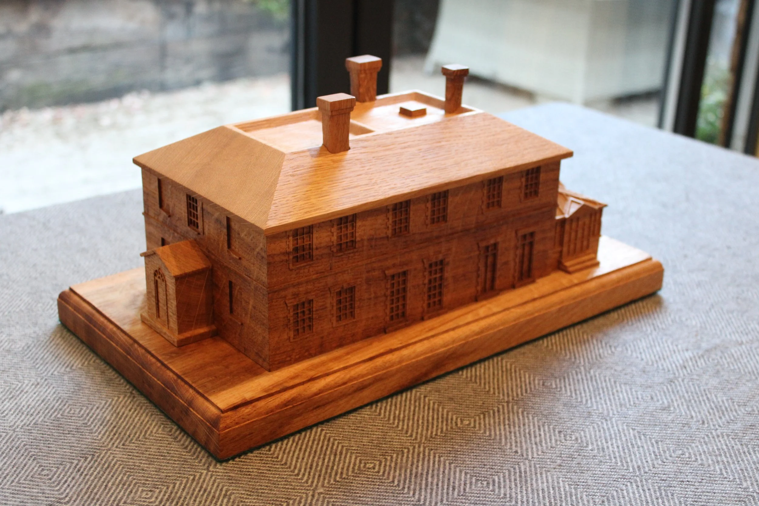Wooden detailed architectural model of a large house or building on a table near a window.