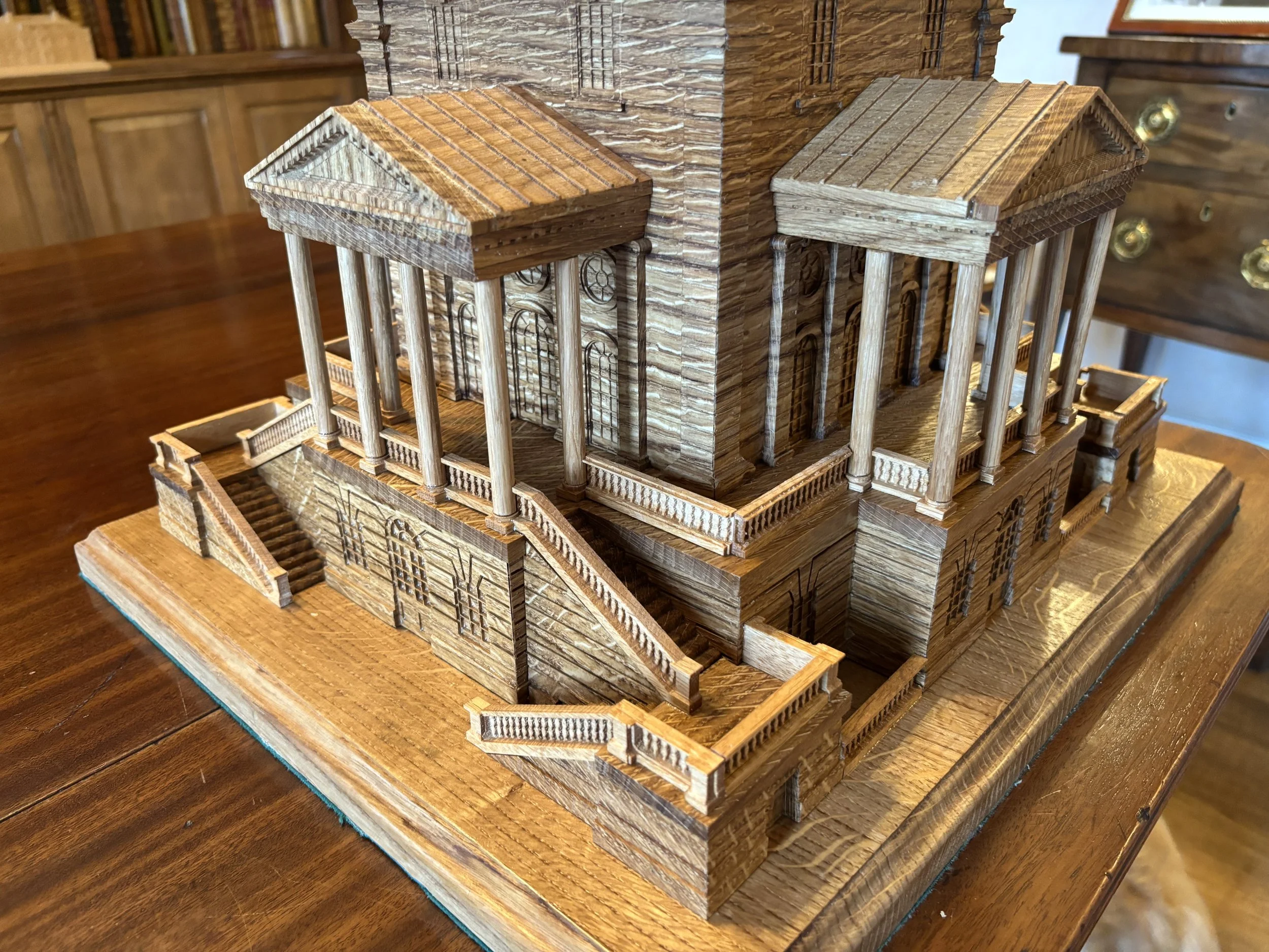Detailed wooden architectural model of a classical building with columns, stairs, and multiple levels displayed on a wooden table.