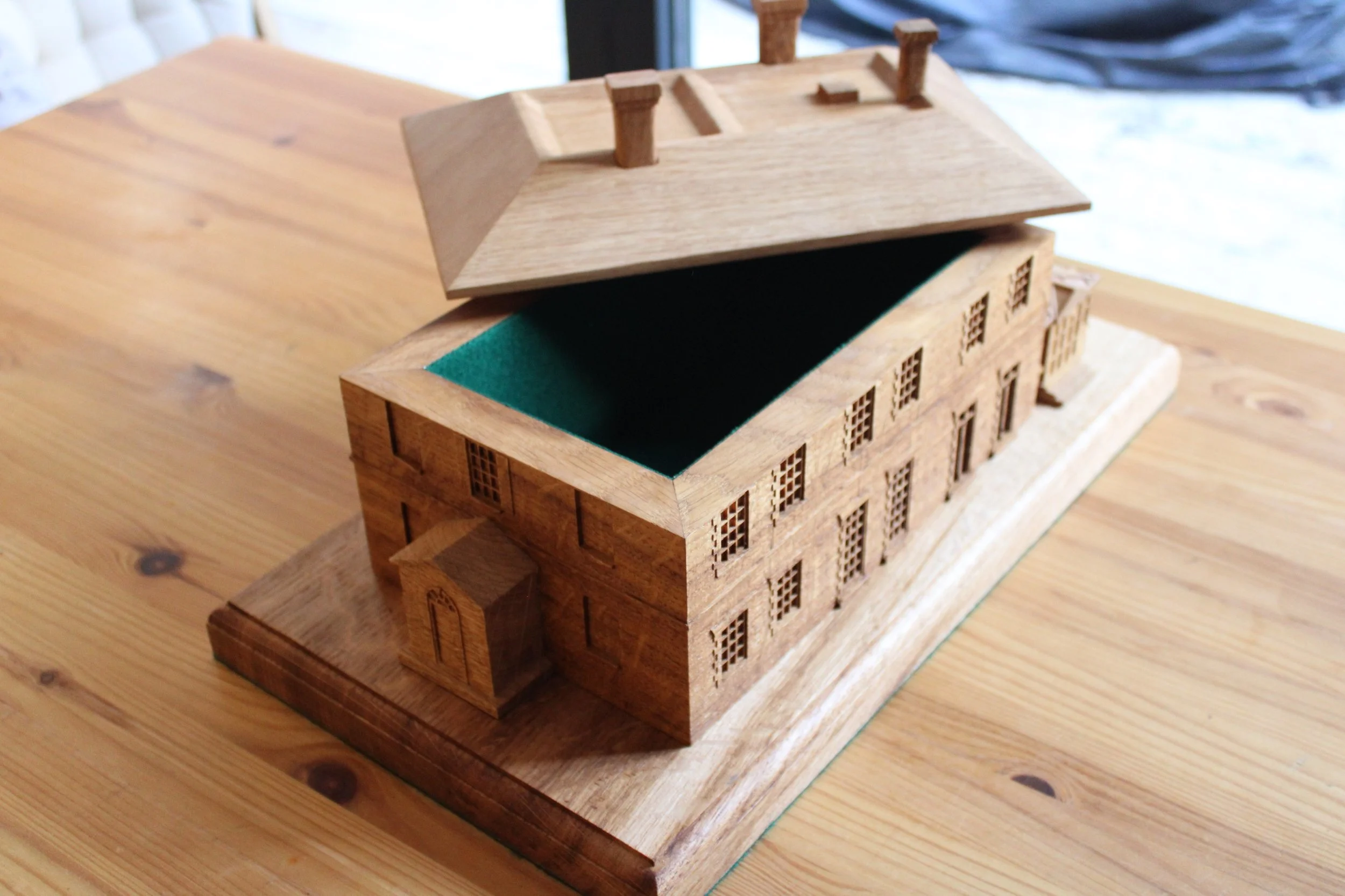 Wooden architectural model of a building with a pitched roof and small porch, resting on a wooden table.