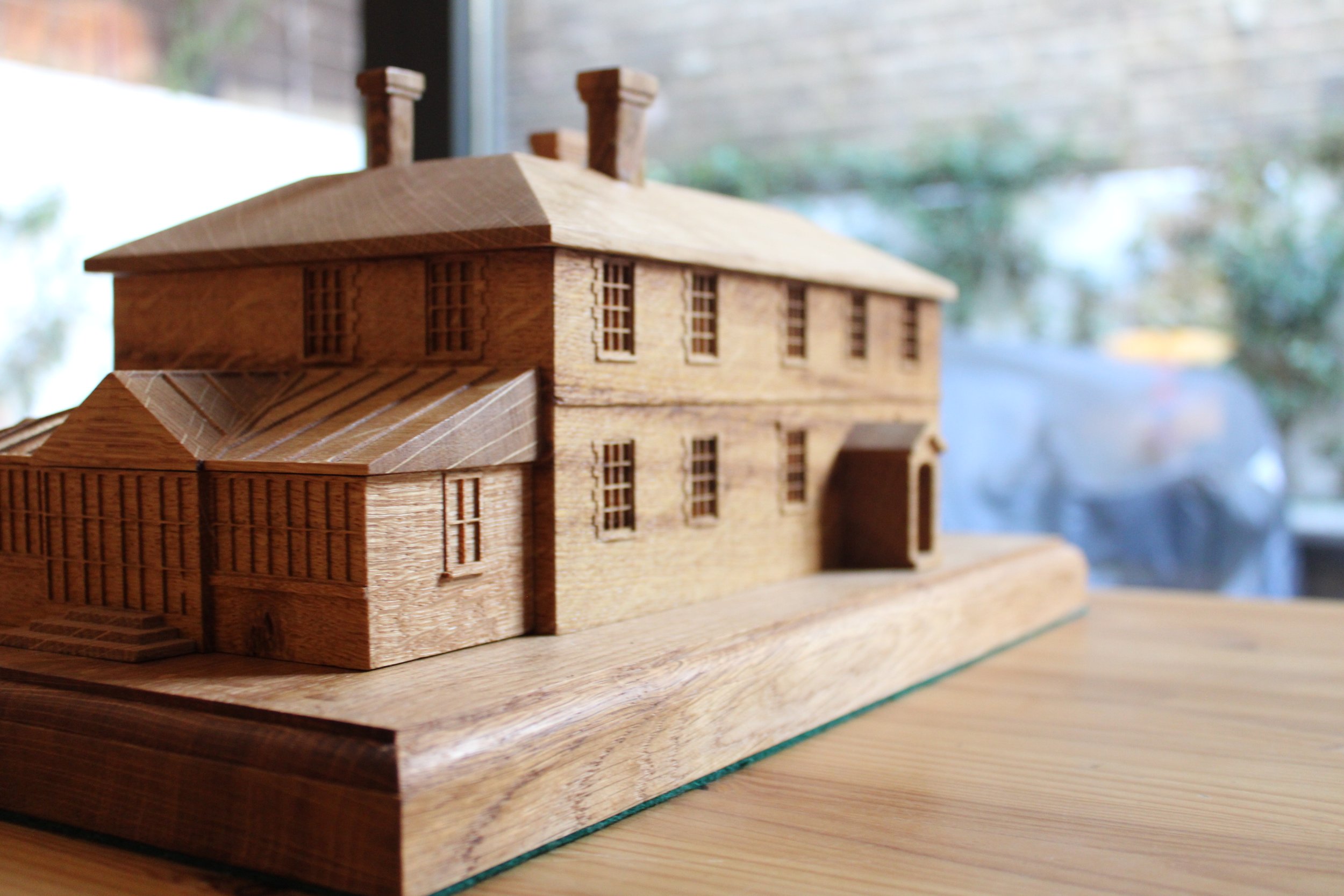 Wooden architectural model of a two-story house with chimneys on a wooden surface.