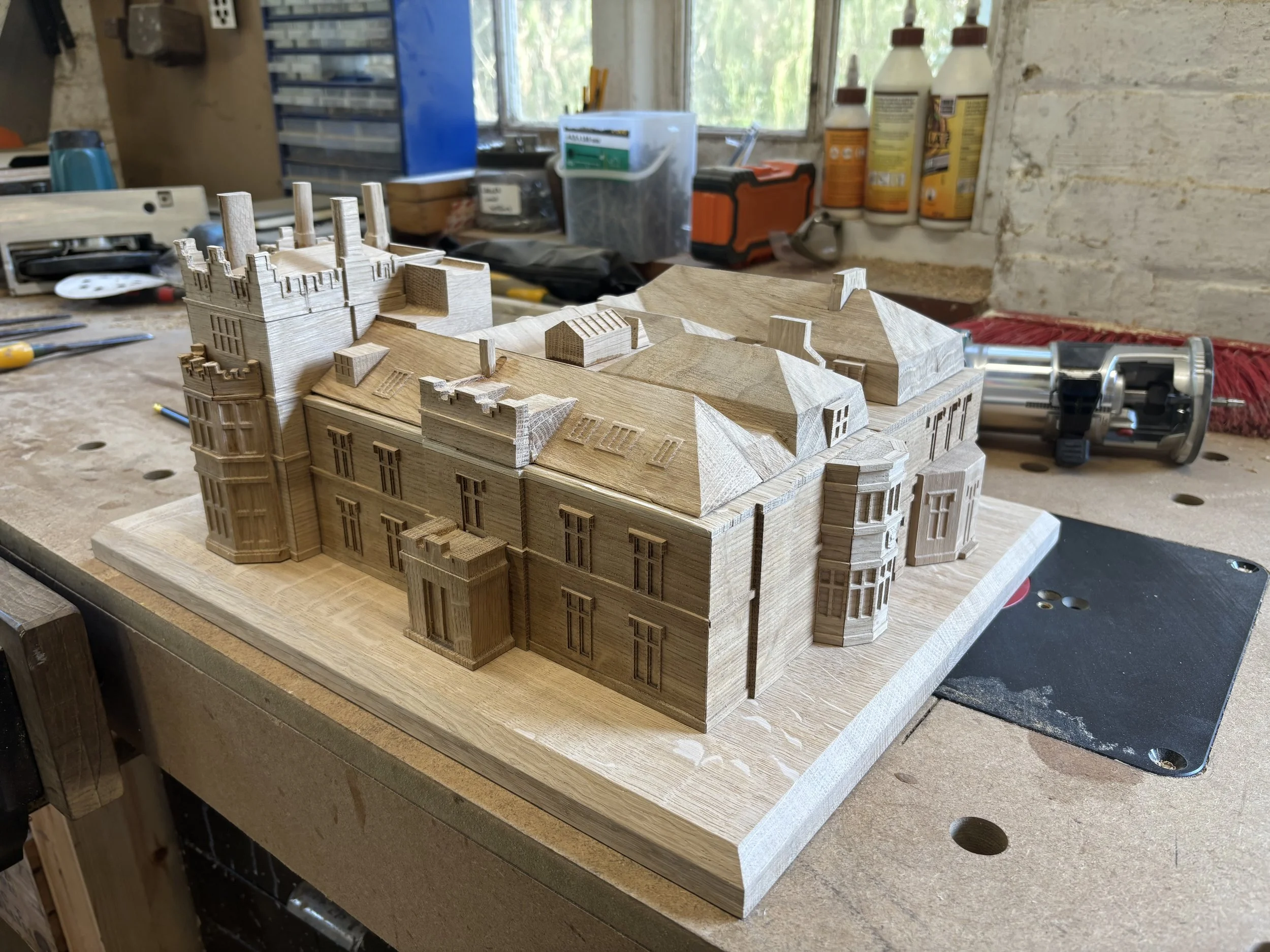 Wooden architectural model of a castle and historic house on workshop workbench.