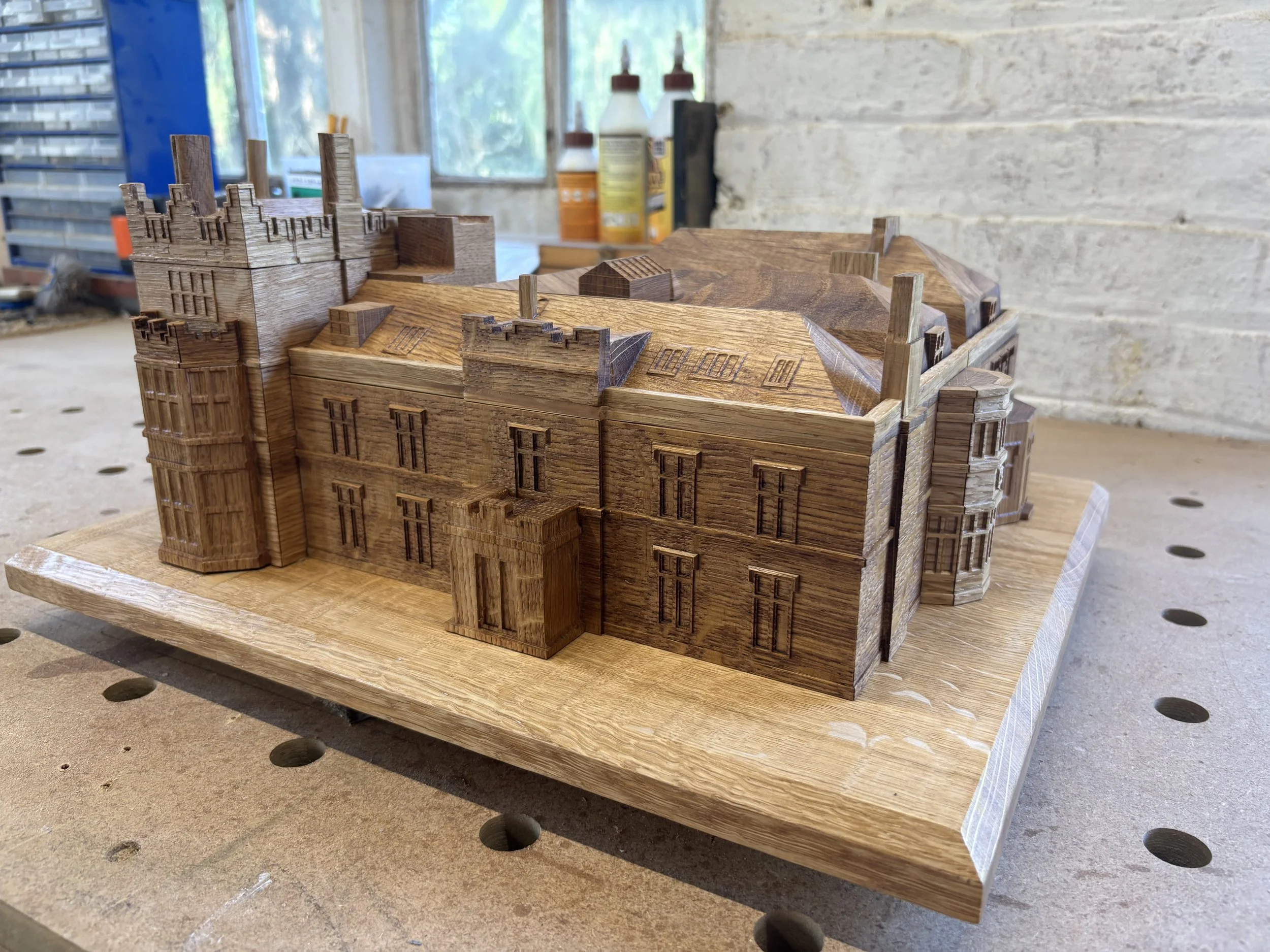 A detailed wooden model of a building with multiple sections, including towers and windows, placed on a workbench in a workshop.