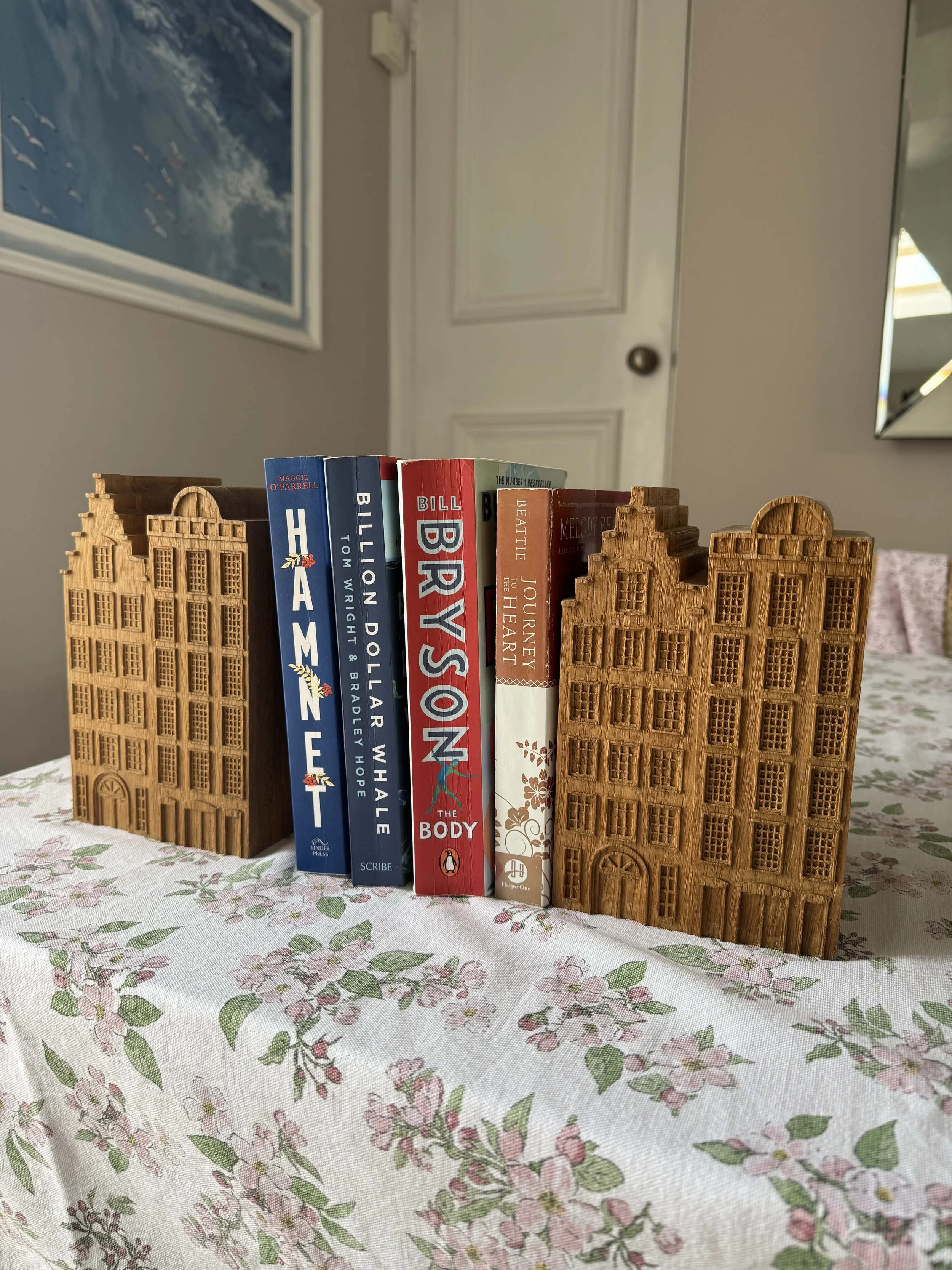 Books standing between two wooden building-shaped bookends on a tablecloth with a floral pattern.