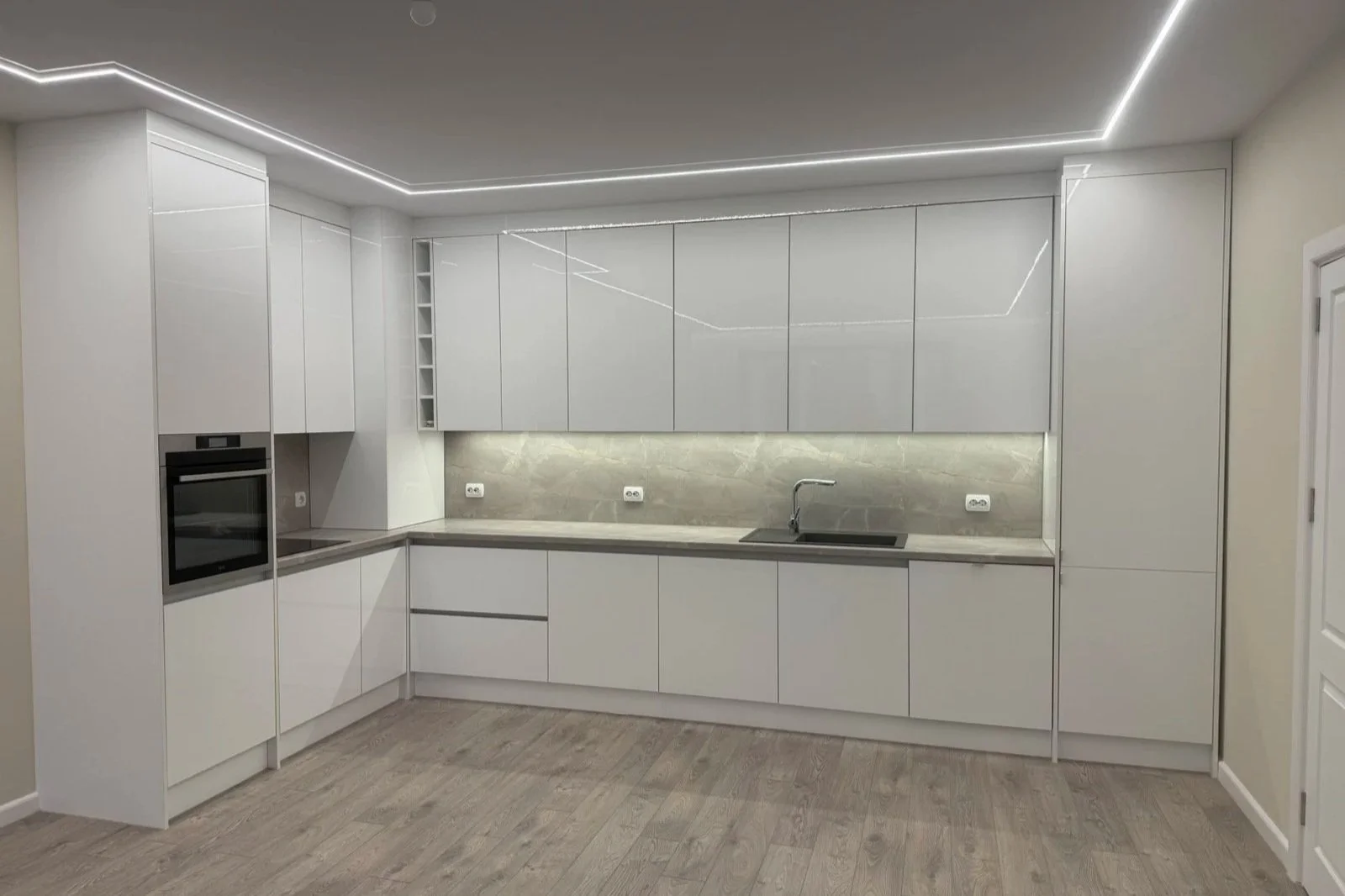Модерна бяла кухня с вградени LED ленти на тавана, термоплот с каменна текстура и бездръжкови механизми.