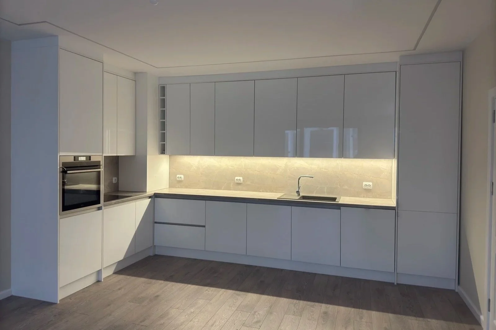 Модерна бяла кухня с вградени LED ленти, термоплот с каменна текстура и бездръжкови механизми.