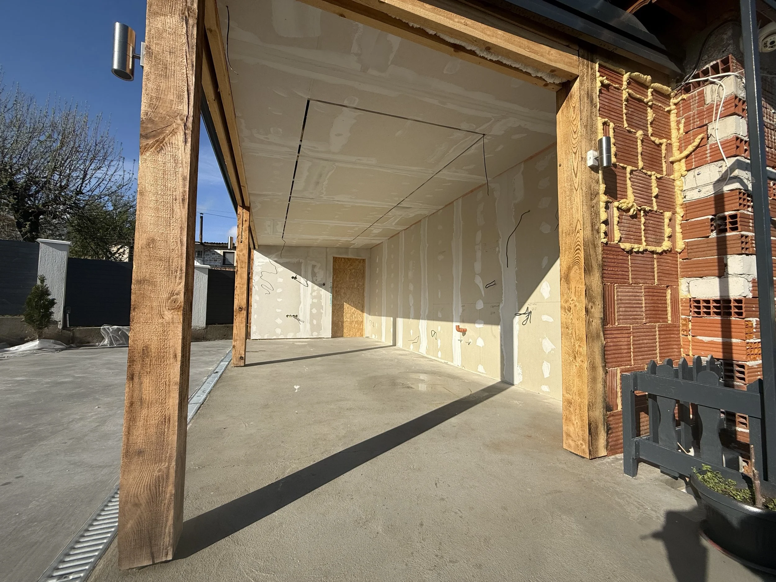 Строителство на малка сграда в Пловдив с дървена конструкция, частично завършена тухлена стена, бетонен под и недовършен интериор с гипсокартон, под ясно синьо небе – строителство и довършителни работи от PDD Luxury Constructions