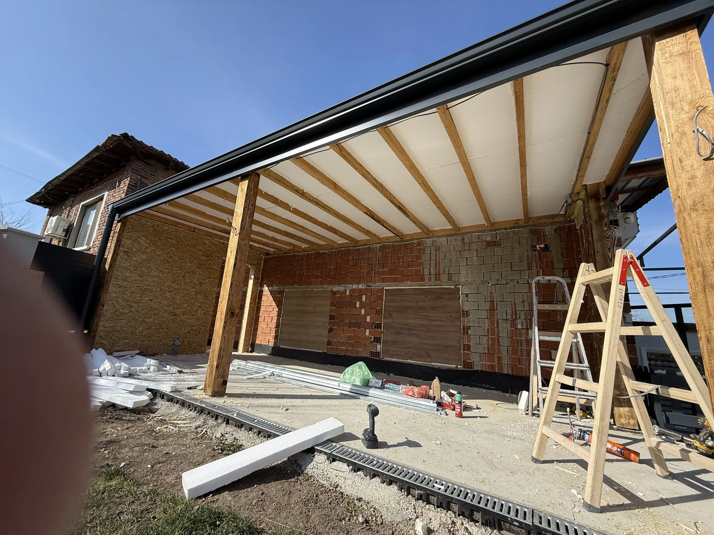 „Строителен обект за веранда в Пловдив с тухлена стена, дървени подпорни греди и частично завършен покрив, инструменти и материали разпилени – строителство и довършителни работи от PDD Luxury Constructions