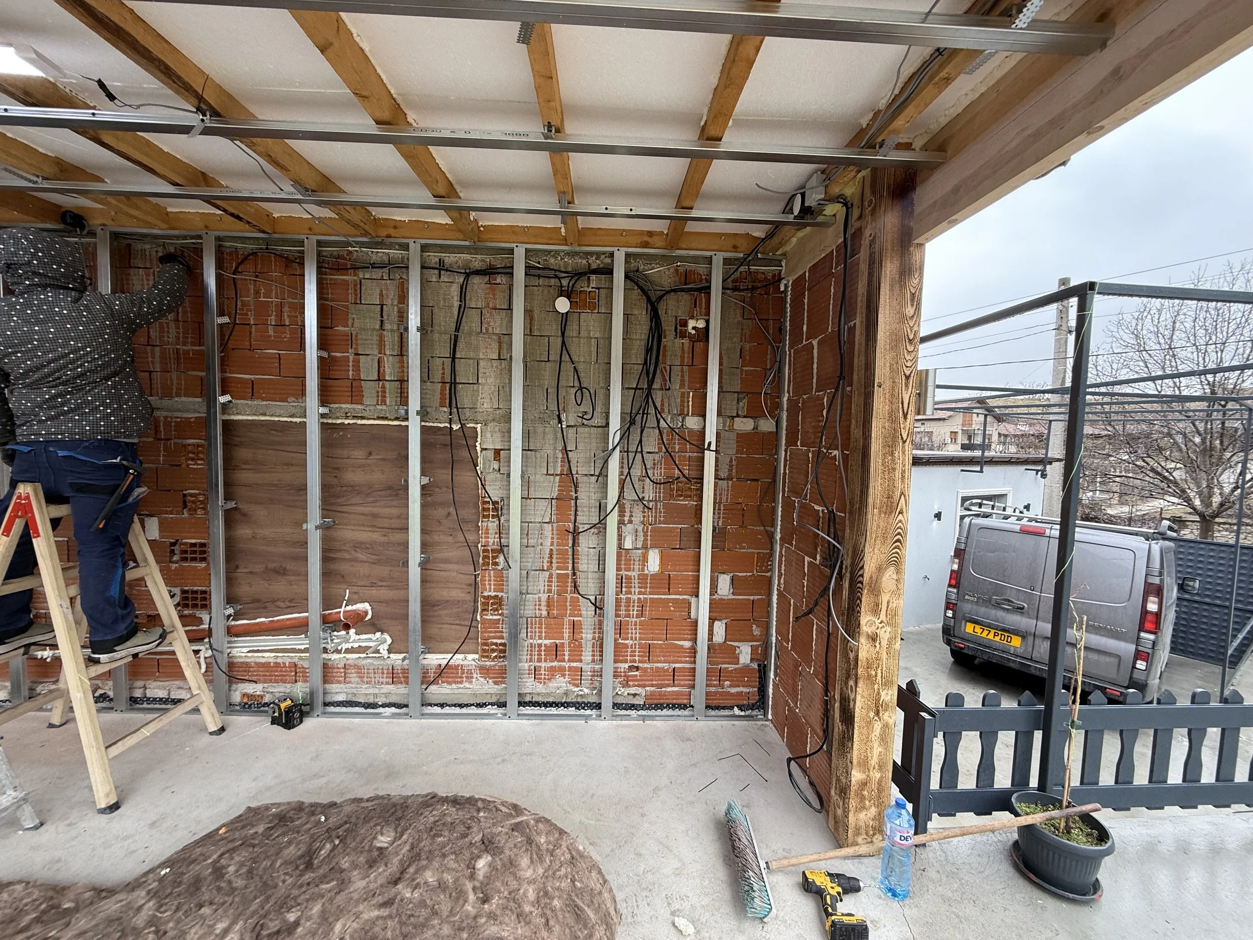 Строителен обект в Пловдив с видими тухлени стени, електрическо окабеляване и метална конструкция, човек на стълба работи, а около него са строителни инструменти и материали – строителство и довършителни работи от PDD Luxury Constructions