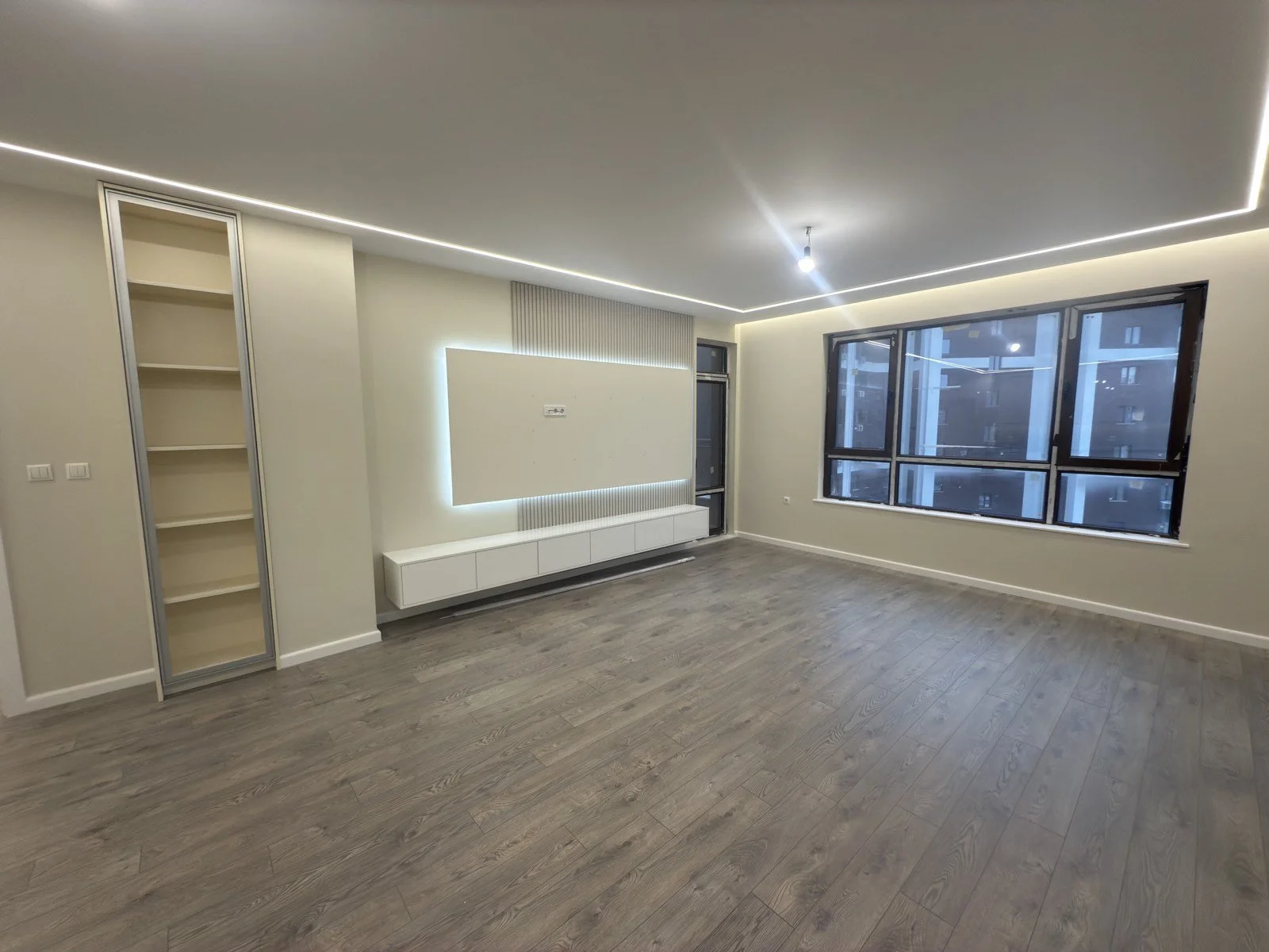 Минималистична ТВ секция с фоново LED осветление, фрезовани панели и светъл ламиниран паркет.