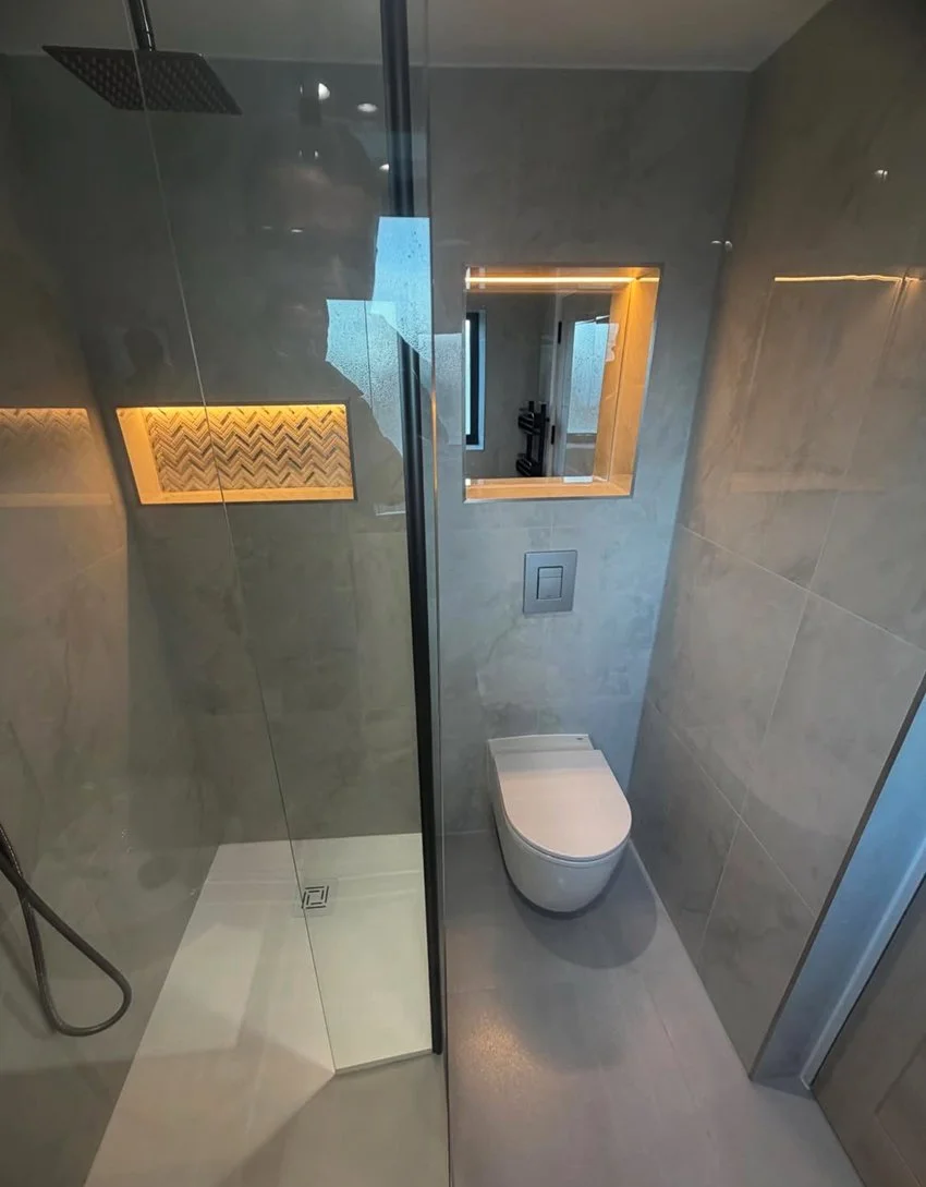 Прецизно изпълнение на вградена тоалетна структура с осветена декоративна ниша и широкоформатни плочки. Wall-hung toilet installation with a recessed LED-lit niche and large-format porcelain tiles.