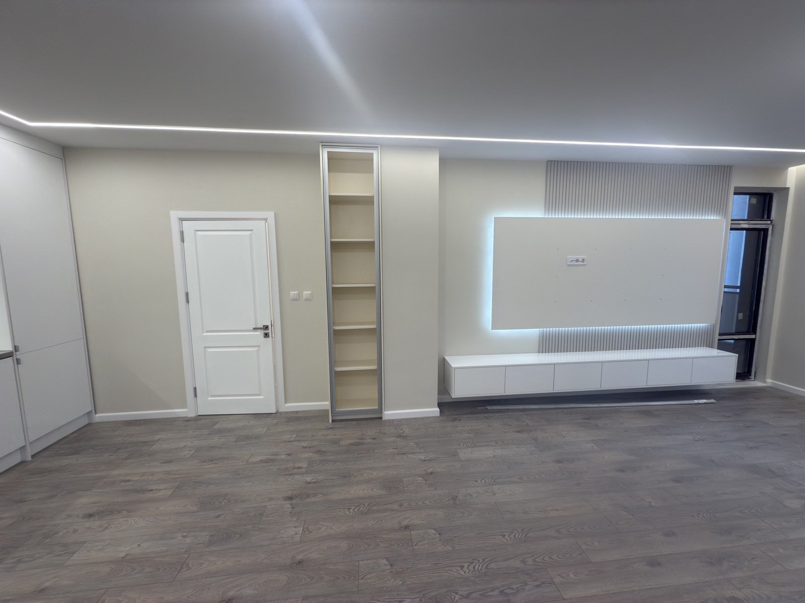 Минималистична ТВ секция с фоново LED осветление, фрезовани панели и светъл ламиниран паркет.