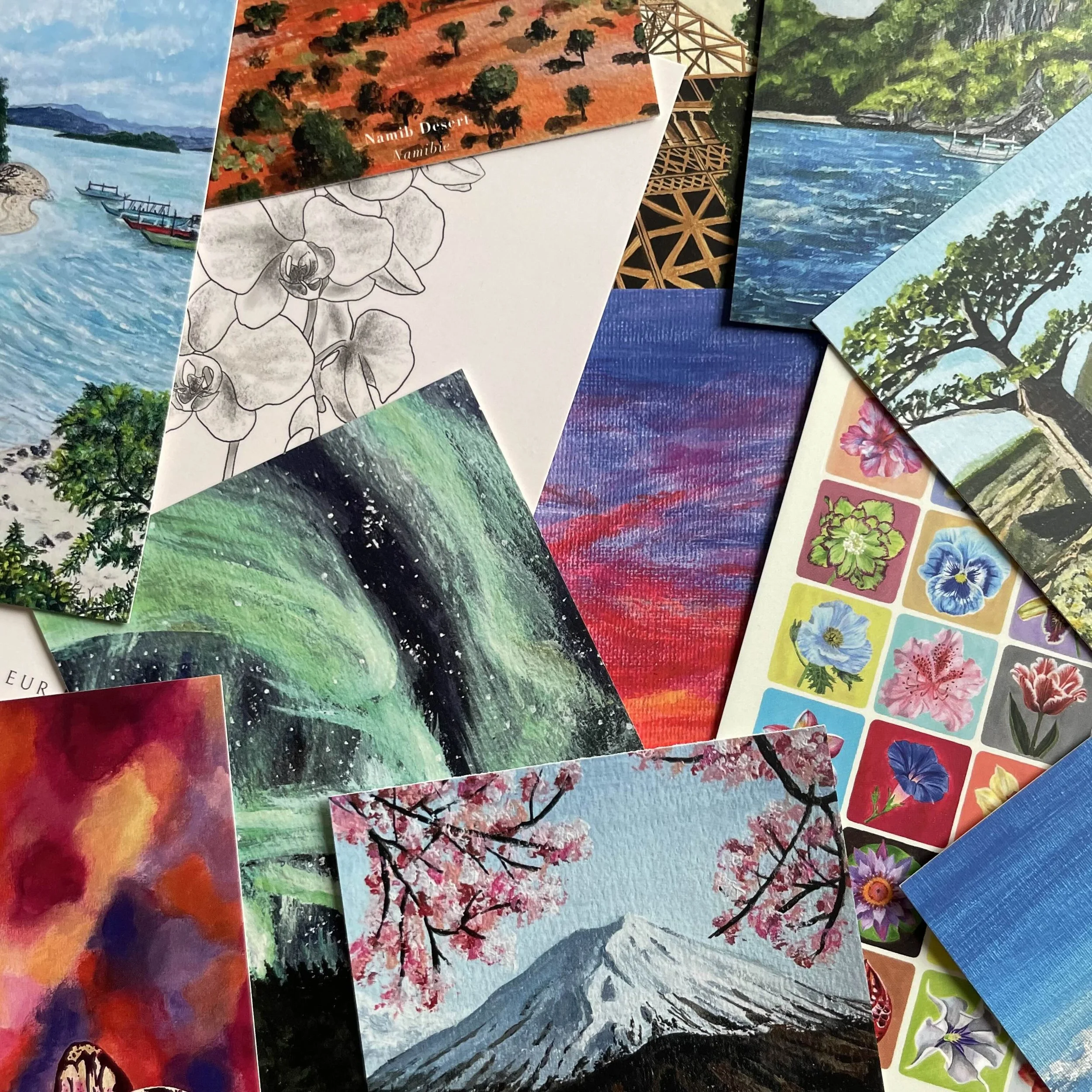 Un assortiment de cartes ou de peintures représentant des paysages variés, y compris des montagnes, des arbres en fleurs, des aurores boréales, une rivière, et des motifs floraux.