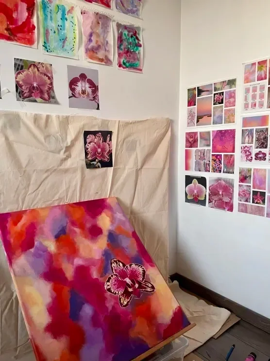 Une pièce avec plusieurs images et peintures de fleurs, principalement d'orchidées, sur les murs et une toile sur un chevalet avec des couleurs vives et un motif de fleur.