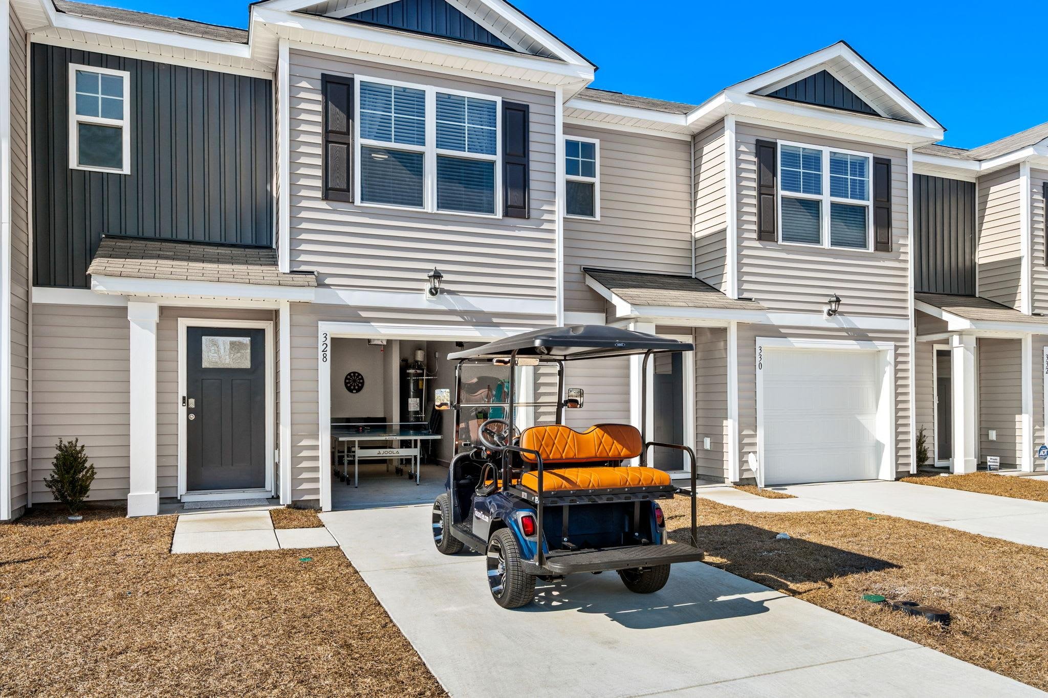 Row of modern townhouses with a golf cart parked in front of one of the driveways, and a game table set up inside the garage.