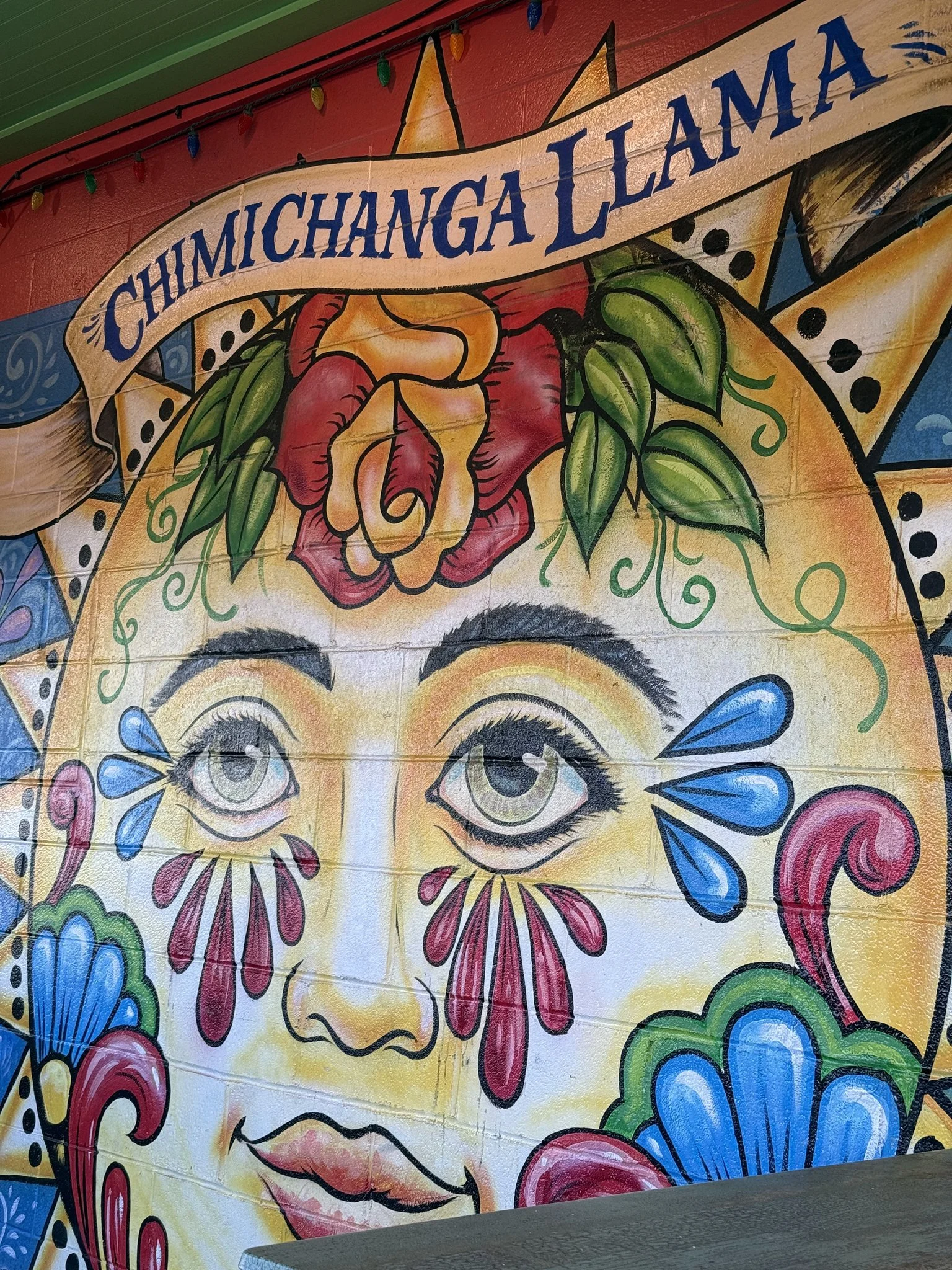 Colorful mural featuring a woman's face with large eyes, floral elements, and a banner reading 'Chimichanga Llama' at the top.