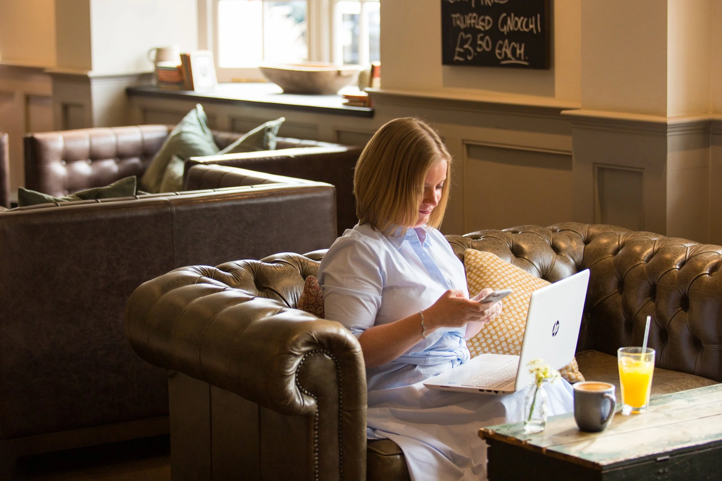 Woman sitting on a sofa with a laptop and phone