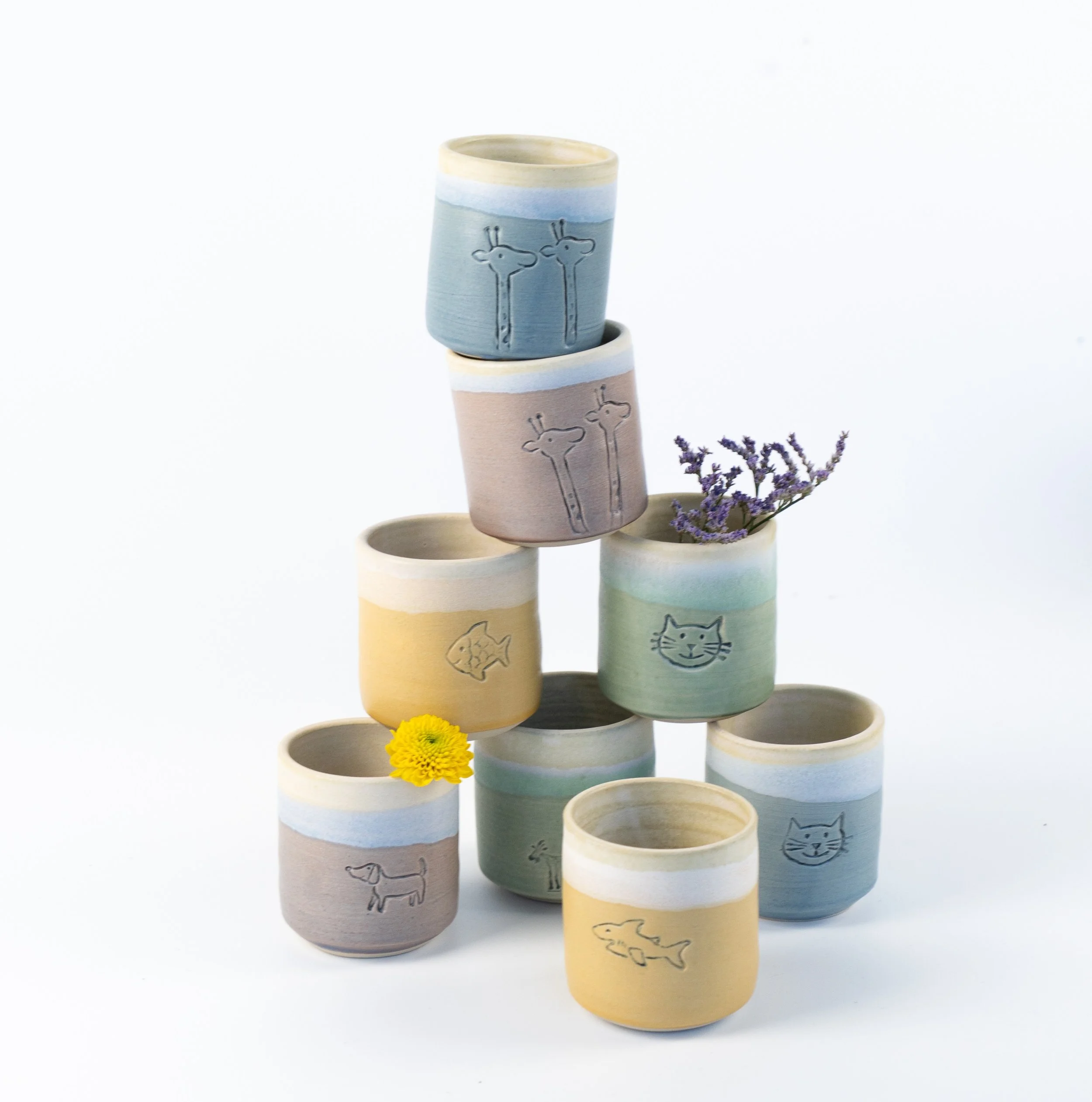 Bunte Schalen mit Tierzeichnungen, darunter Frosch, Krebs, Hase, Ziege, Delfin, Biene, Schildkröte, Eidechse, Fische, Gürteltier, Katze, Vogel, Hund, Frösche, und andere Tiere auf einer weißen Tischdecke.