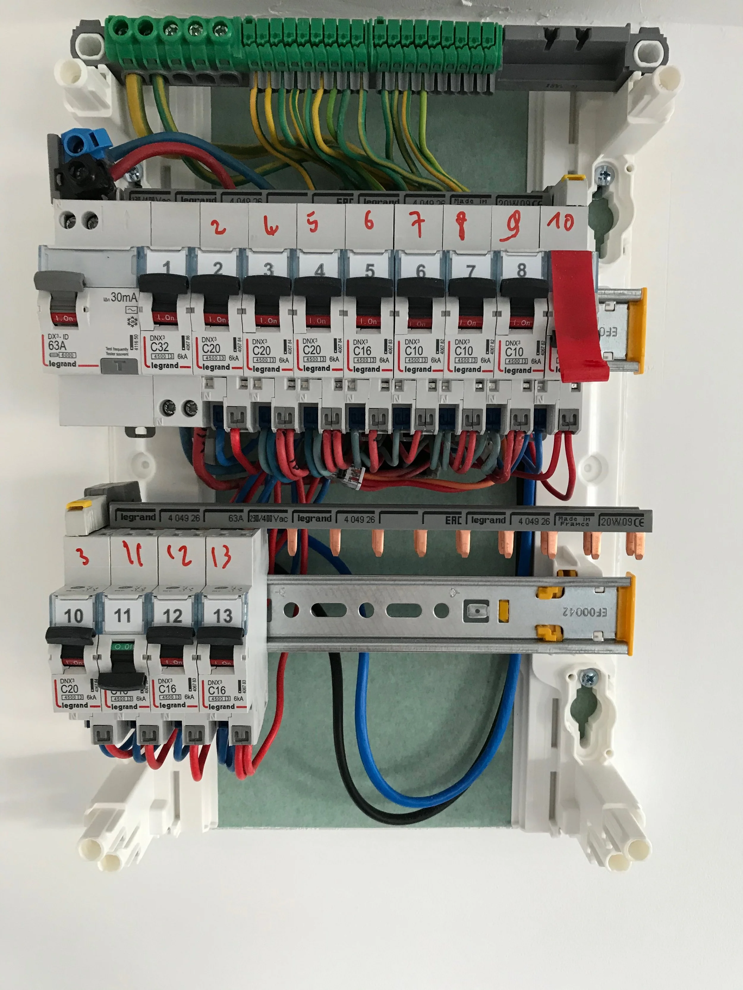 Tableau électrique avec des disjoncteurs et fils électriques connectés, avec instructions écrites en rouge à la main indiquant des numéros.