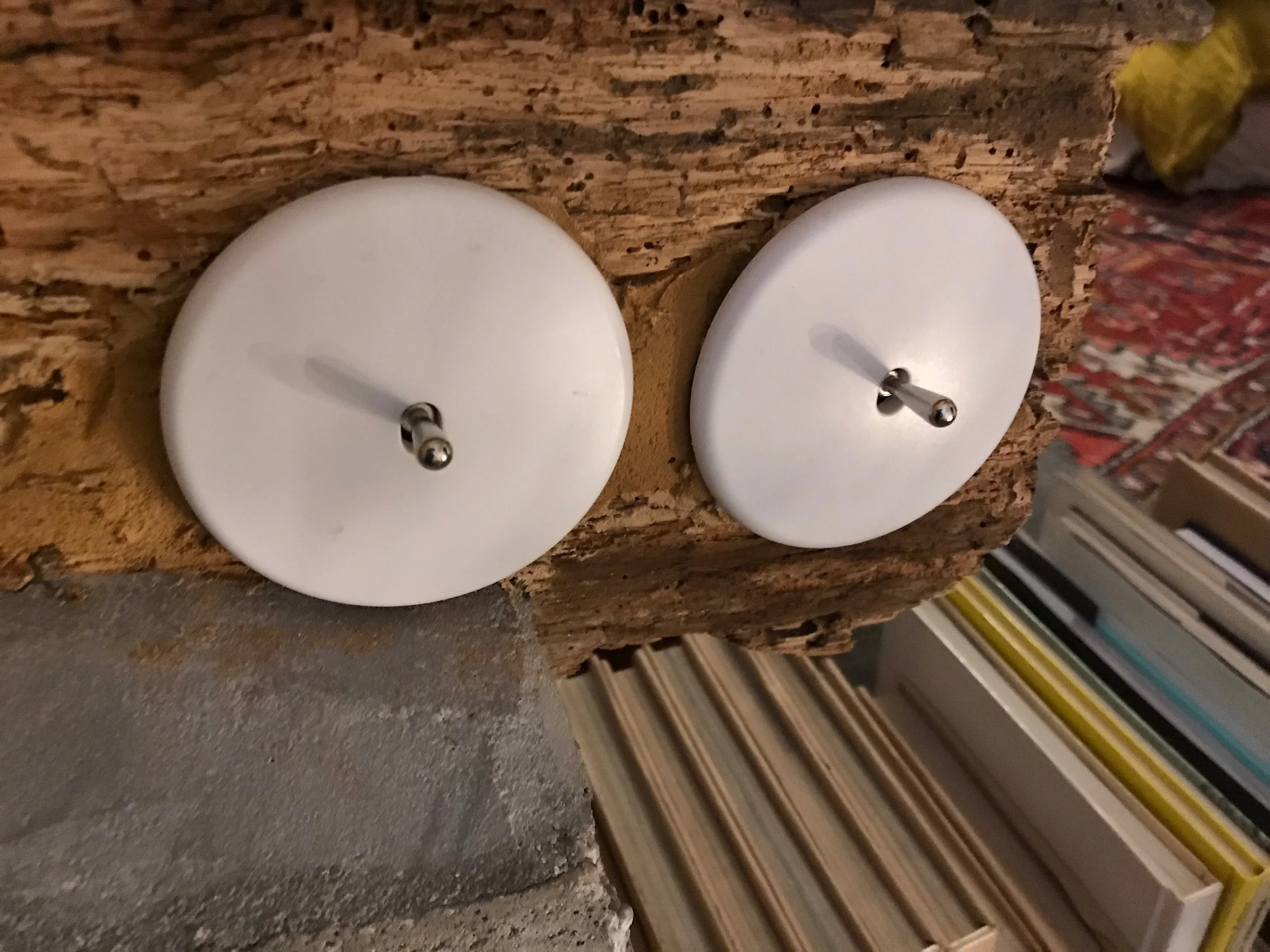 Deux bougies blanches rondes sur un support en bois, avec un fond montrant des livres et autres objets.