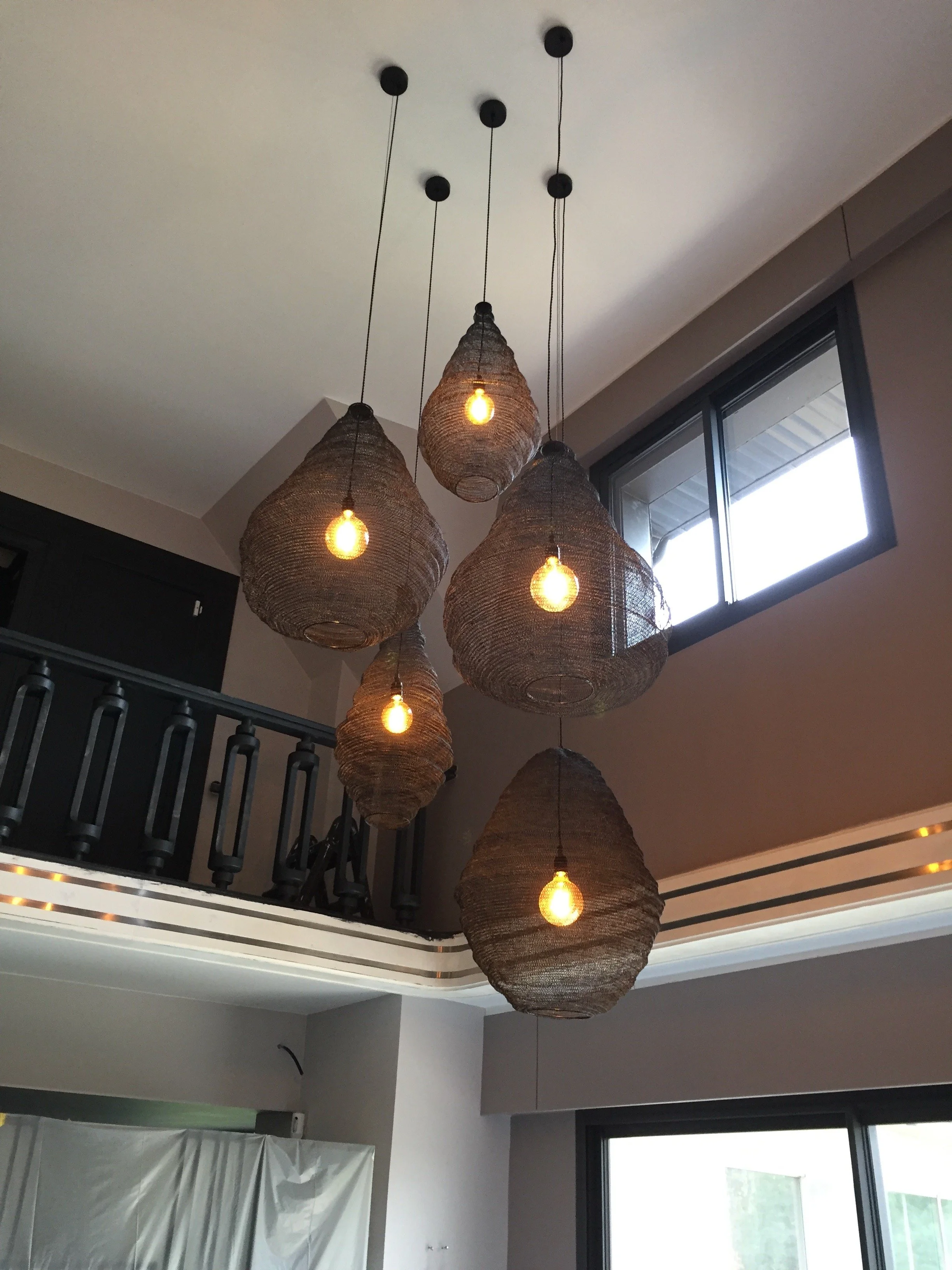 Lustre suspendu avec plusieurs abat-jour en bois tressé. Il y a sept ampoules éclairant le plafond dans un intérieur moderne avec fenêtres.
